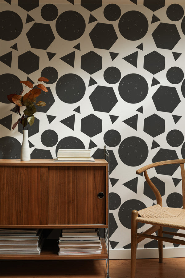 Self-adhesive wallpaper with a geometric pattern of circles, triangles, and hexagons in black and gray against a cream background, in a room with a wooden sideboard and chair.