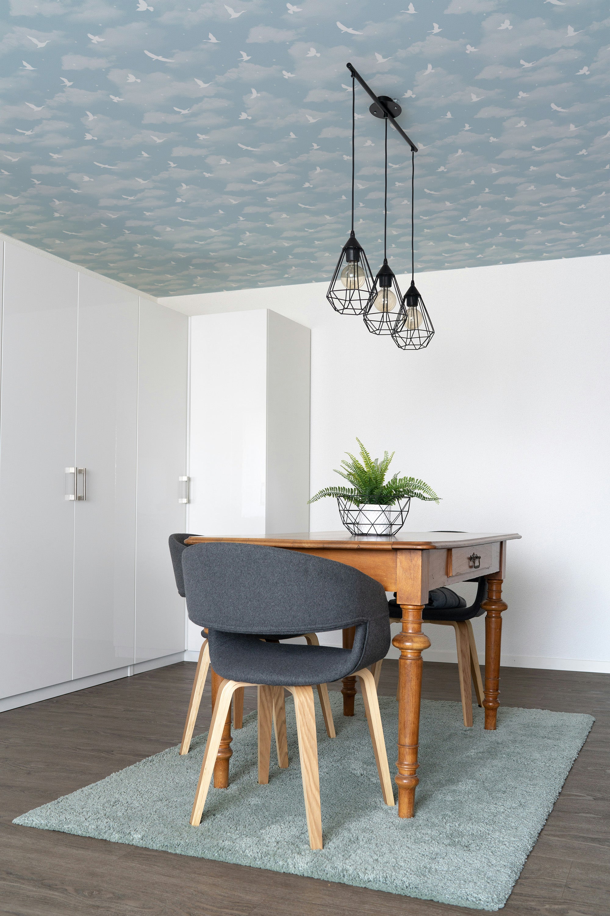 Dining room with wooden table, gray chairs, and decorative ceiling lights.
