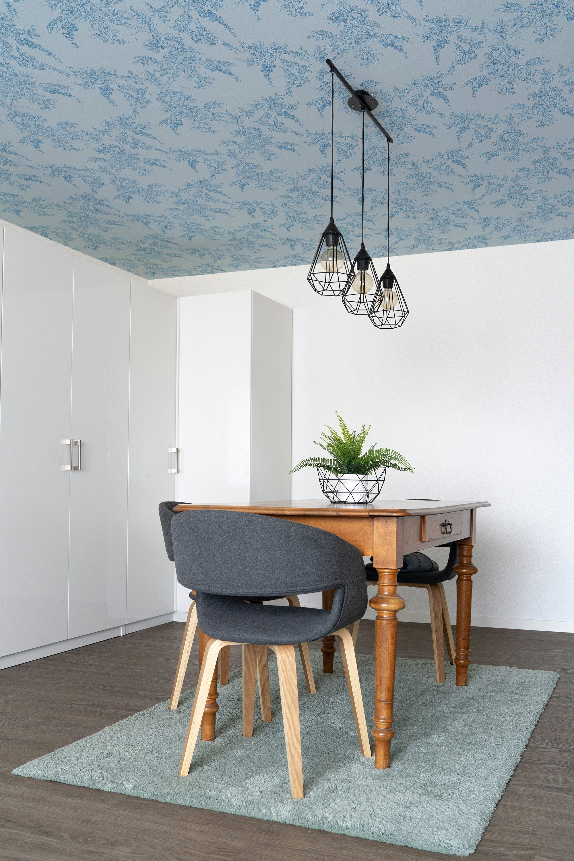Dining room with a wooden table, gray chairs, and blue ceiling wallpaper.