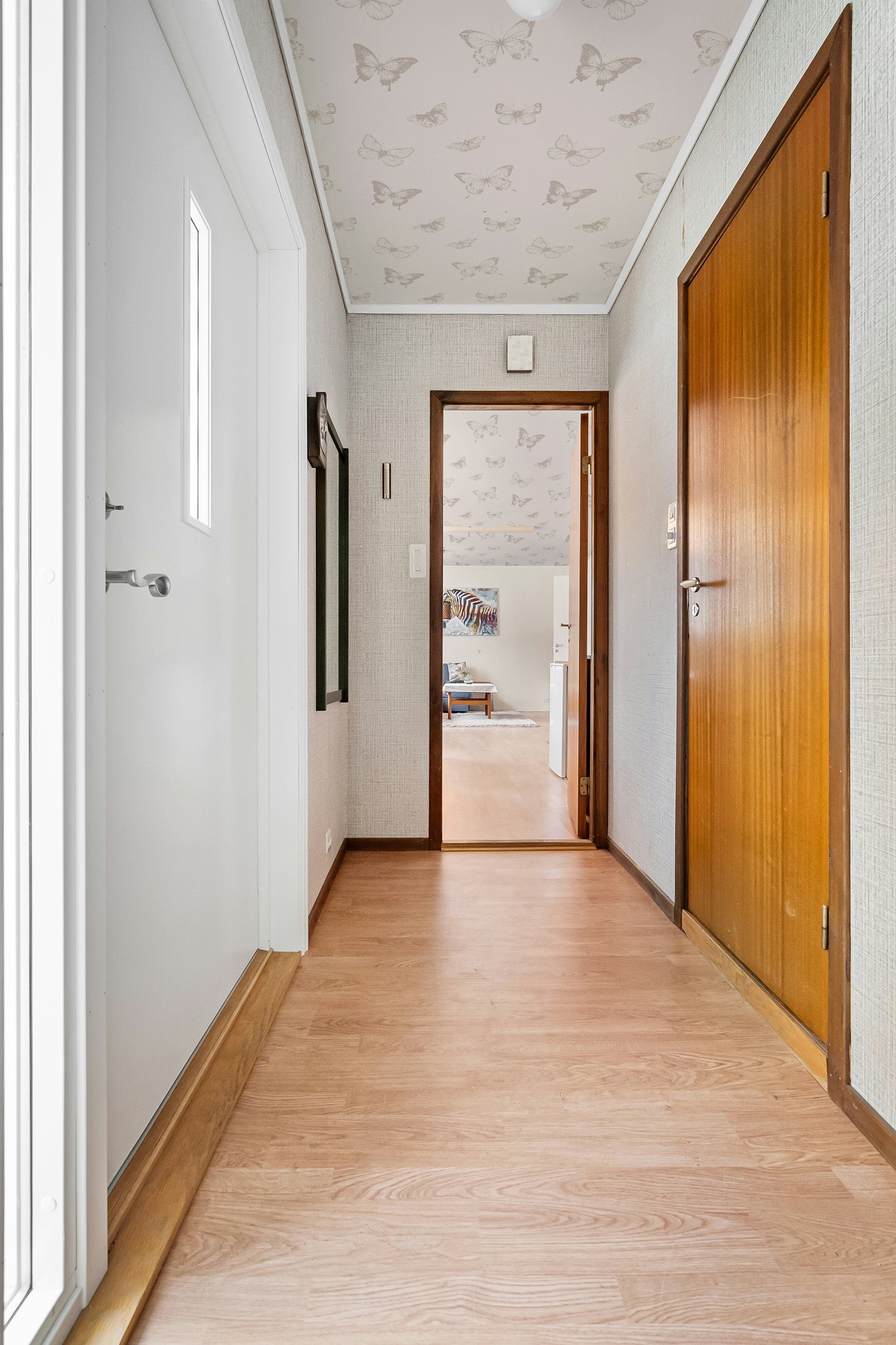 Hallway with wooden floor, white walls, wooden door, and ceiling wallpaper.