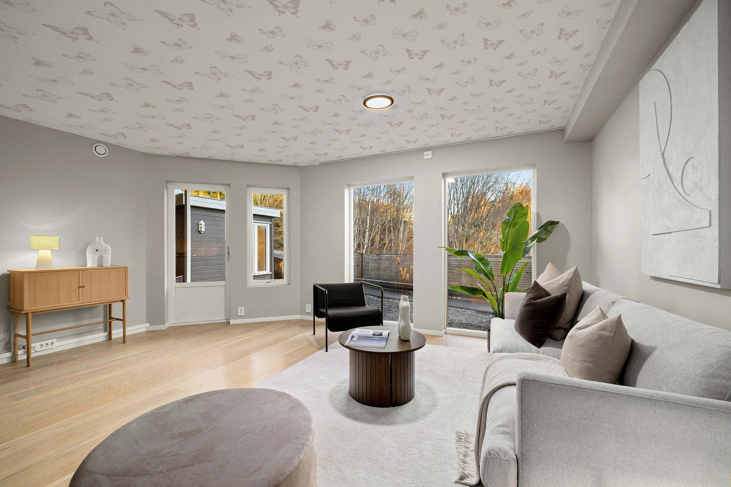 Modern living room with a gray sofa, a black armchair, and a butterfly ceiling. 