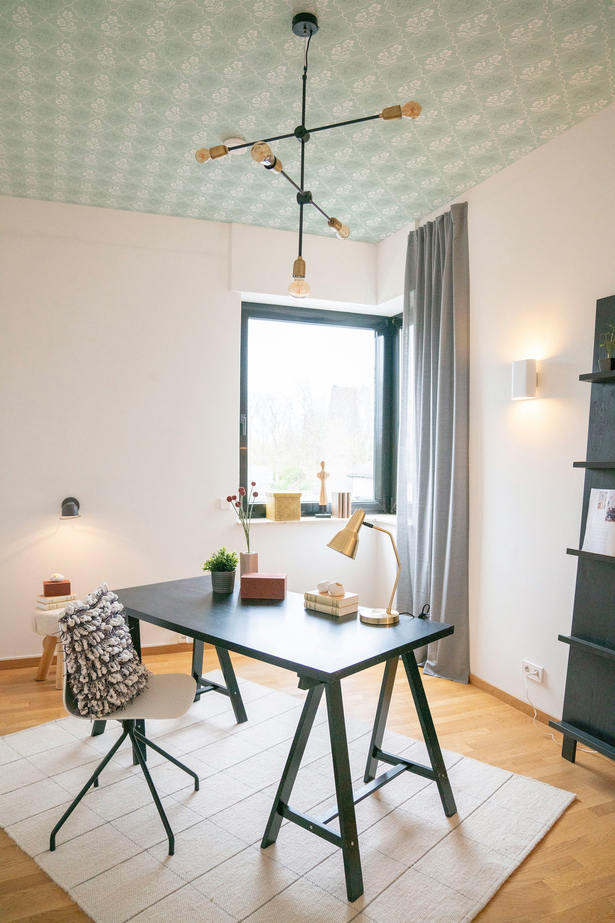 Modern home office with a desk, chairs, decorative elements, and green ceiling wallpaper.