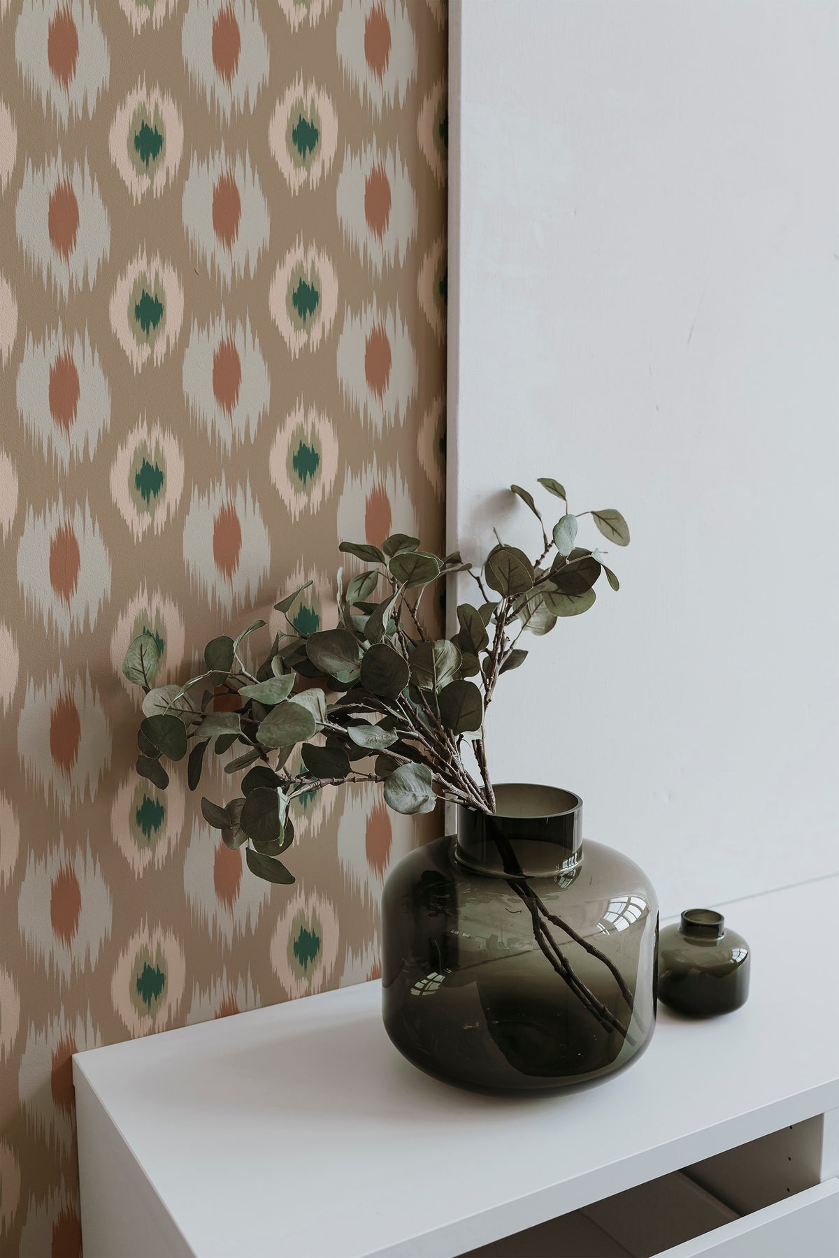 Jagged Ikat Ovals grasscloth wallpaper on an interior wall, tan ground with jagged oval motifs in green and rust.