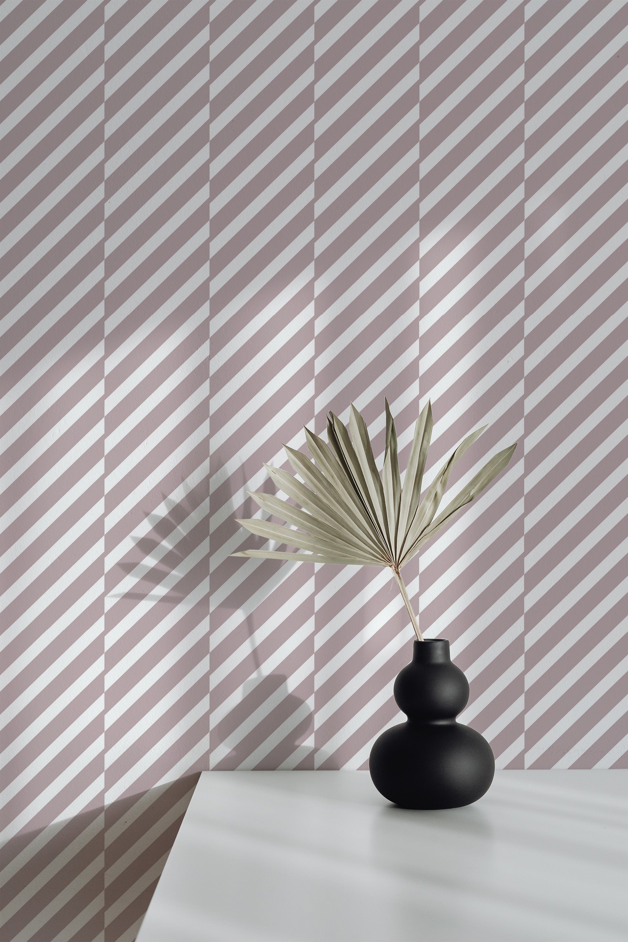 Self-adhesive wallpaper with a modern diagonal stripe pattern in alternating shades of white and light taupe, covering the wall behind a black matte vase with a dried palm leaf.