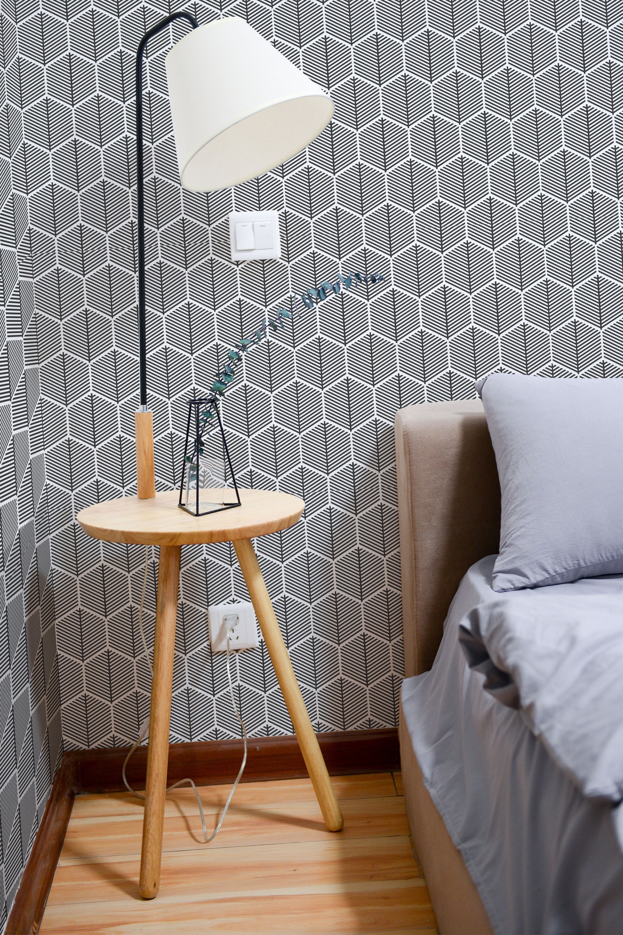 Self-adhesive wallpaper with a geometric honeycomb pattern in contrasting shades adorning the wall of a modern bedroom.