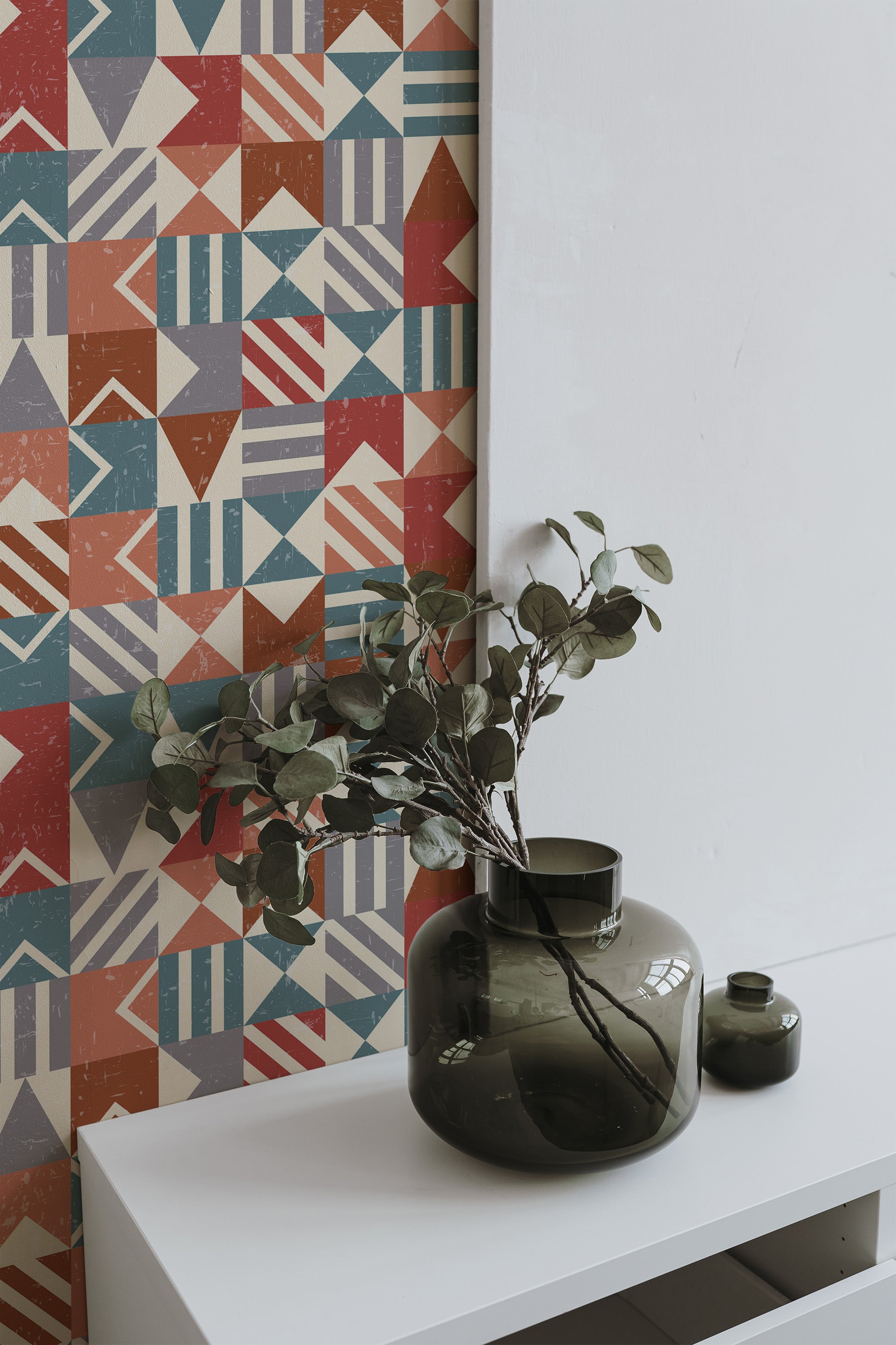 Self-adhesive geometric wallpaper with a vintage-inspired design in muted tones of red, blue, orange, and green, evoking a retro and artisanal feel with overlapping triangles, stripes, and rectangles of varying sizes and textures.