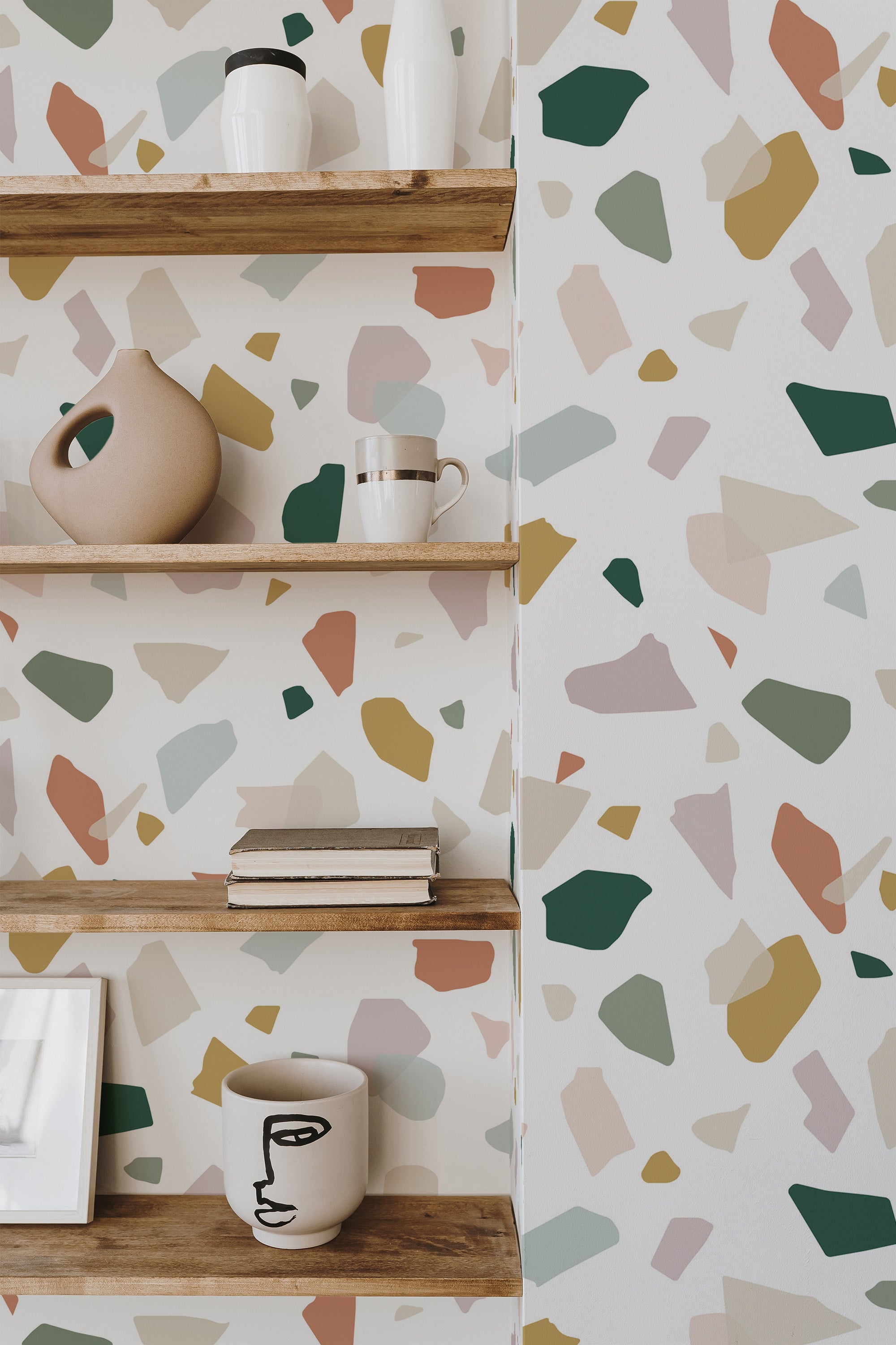 Self-adhesive pastel terrazzo wallpaper with an abstract pattern of irregular shapes in soft colors like beige, olive green, mustard, pink, and off-white on a light background.