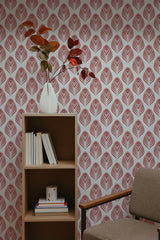 Self-adhesive wallpaper with a repeating red peacock feather pattern on a white background, complementing the room's decor with a brown shelving unit, books, vase, and a plant.