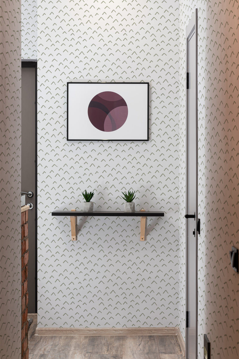 A room with Chevron up patterned wallpaper, characterized by small, repetitive chevron-like shapes in a subtle, minimalist design. Framed artwork and a small shelf with plants adorn the wall with traditional wallpaper.