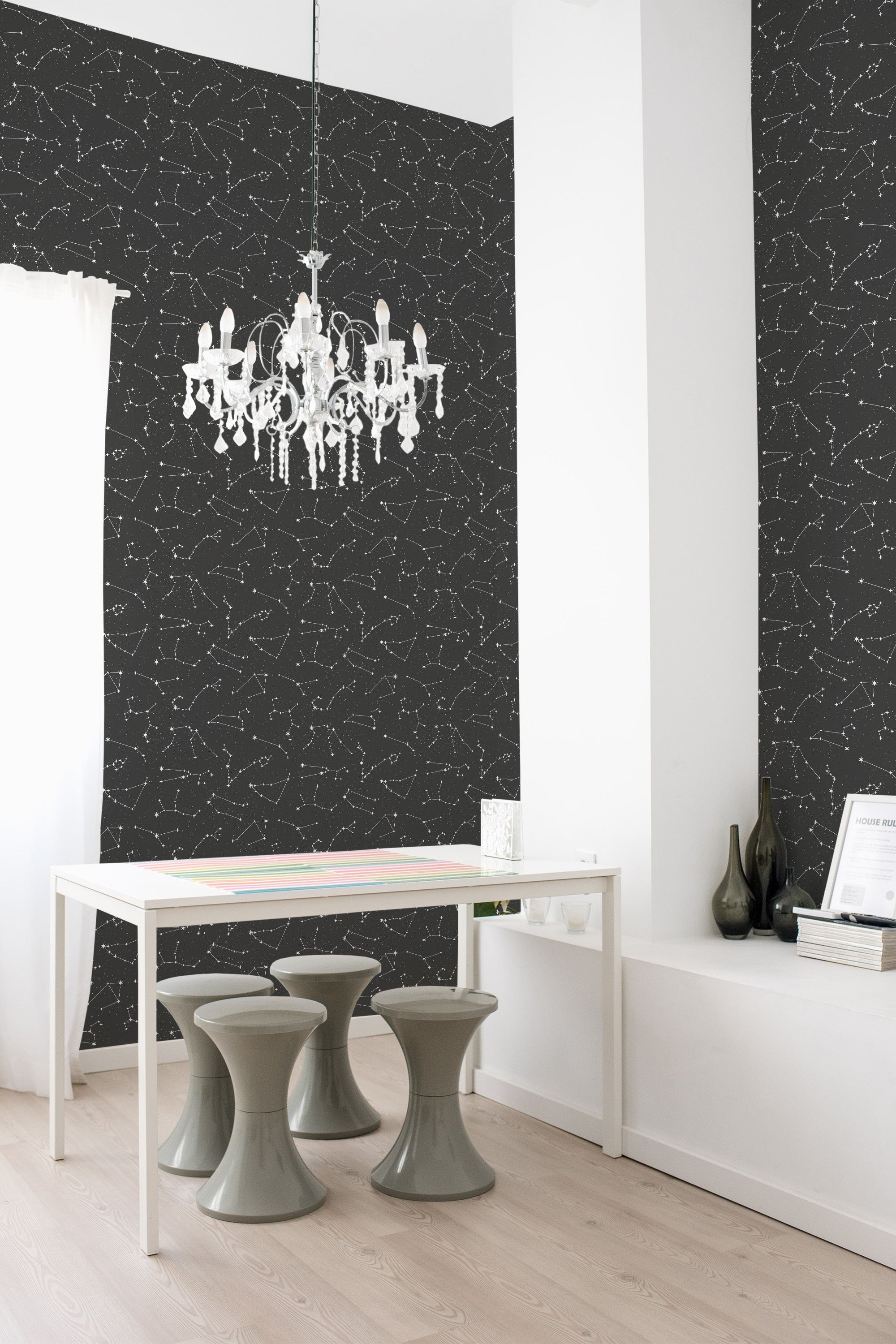 A black wallpaper adorned with white and teal star constellations scattered throughout the design, creating a celestial and cosmic ambiance in the room. The wallpaper adds an intricate, whimsical touch, complementing the minimalist white furniture and light wooden flooring. Traditional wallpaper.