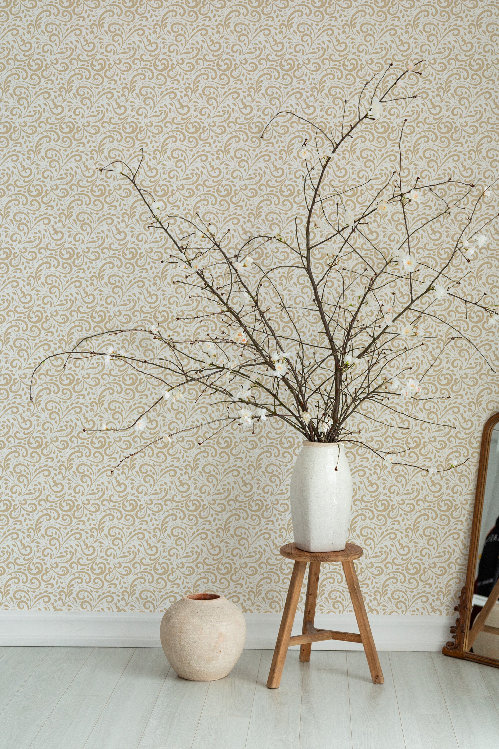 Self-adhesive vintage ornament wallpaper with elegant swirling patterns in beige and gold tones on a light background, complemented by minimalistic decor elements including a white ceramic vase with branches, a small stool, and a mirror leaning against the wall.