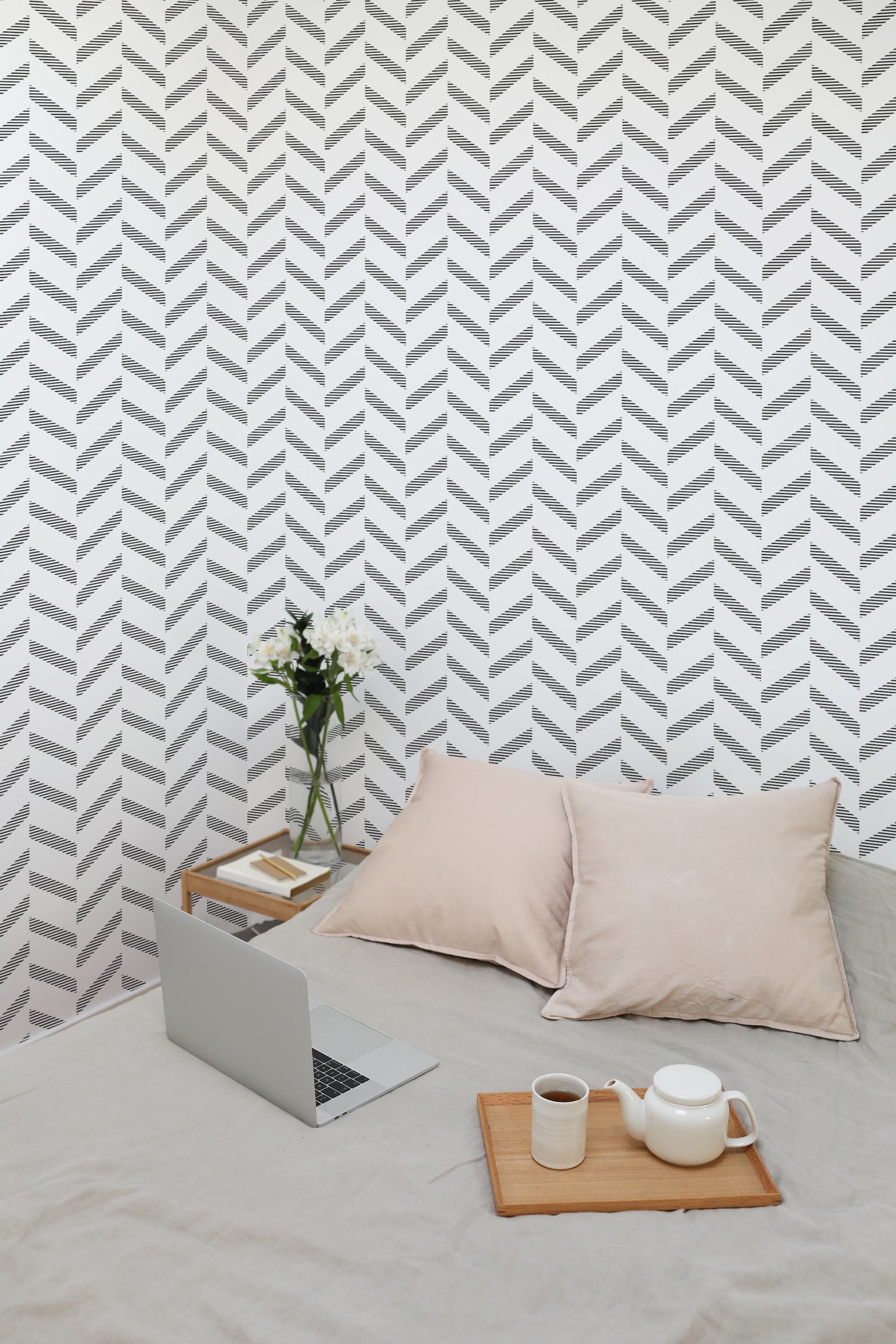 Self-adhesive wallpaper with a striped herringbone pattern in alternating shades of grey and white, installed above a bed with neutral-colored pillows.