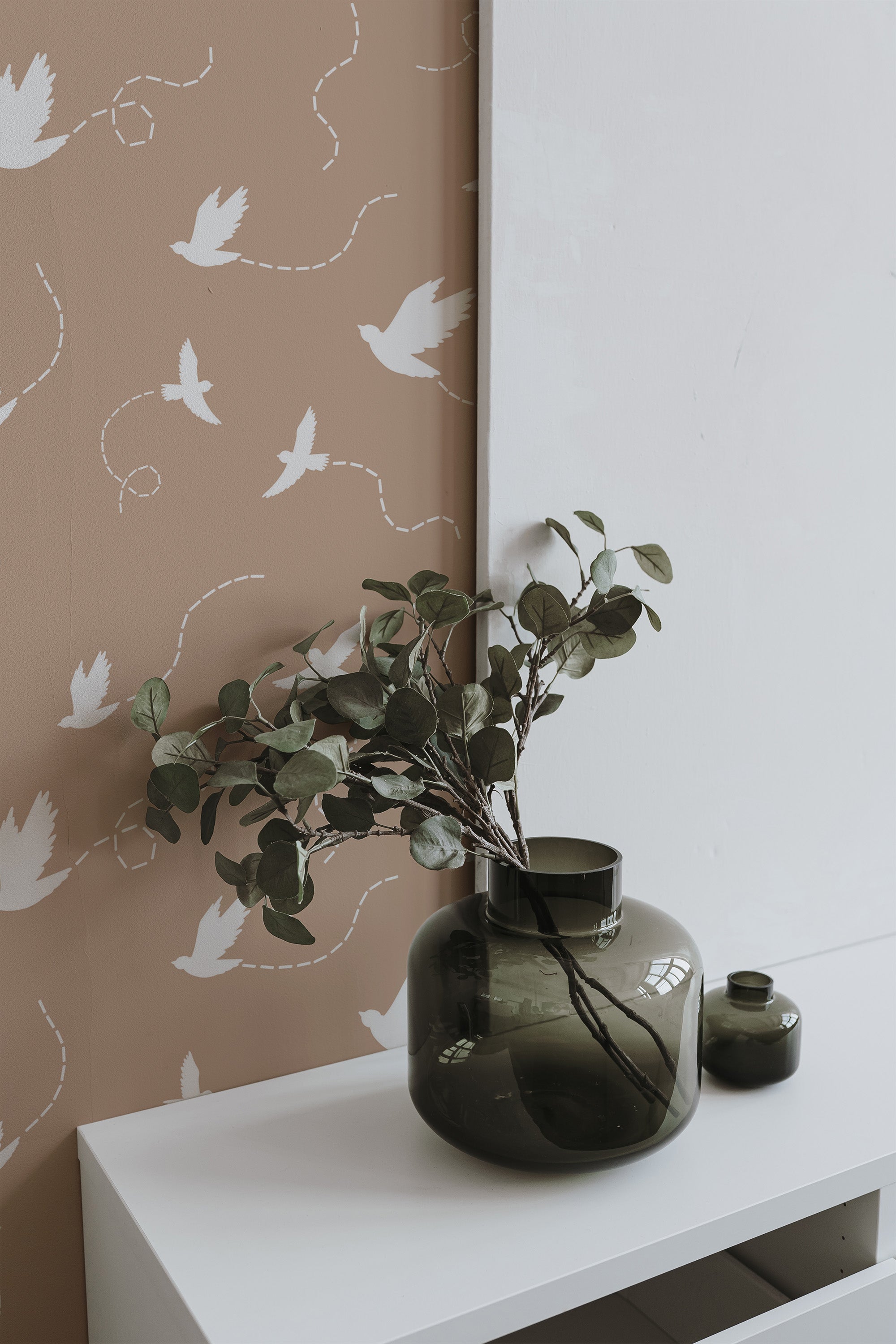 Self-adhesive wallpaper with a Flying Birds design, set against a muted brown background. The pattern includes delicate white birds in various flight directions with dotted lines trailing, giving a sense of movement and whimsy.