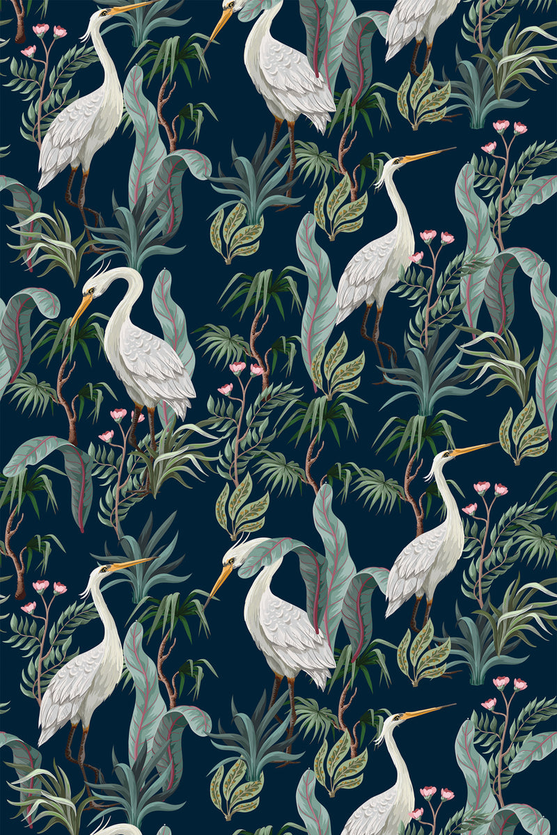 Elegant wallpaper design with white cranes standing among lush green foliage and delicate pink flowers on a dark blue background. Peel and stick removable wallpaper.