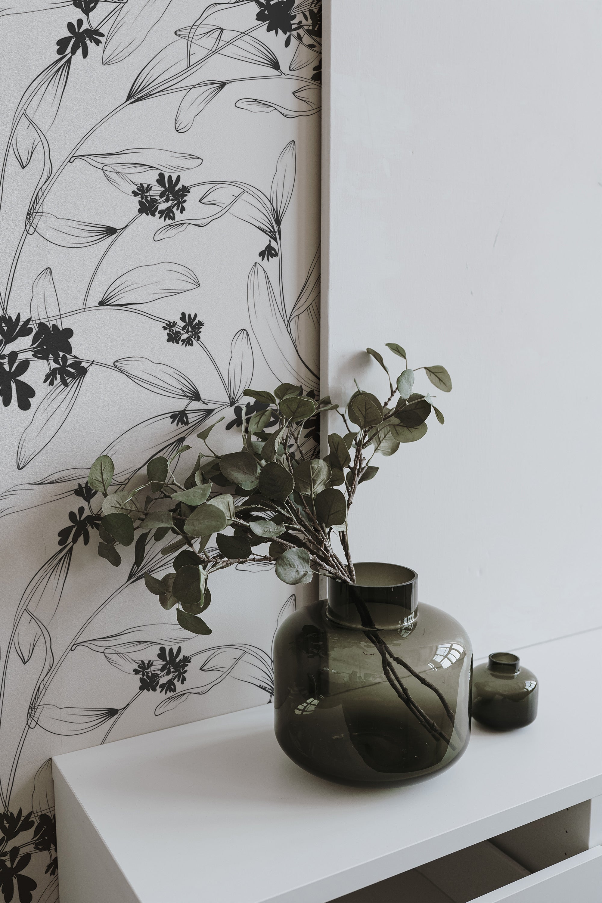 Self-adhesive wallpaper adorned with black and grey floral outlines and leaves against a light background, adding a minimalist, botanical touch to the room.