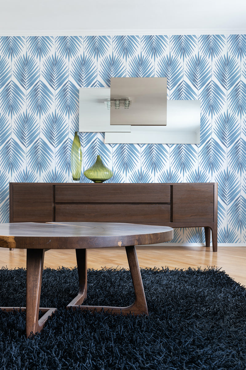 A room with blue and white Farmhouse leaf patterned wallpaper, a wooden sideboard, a round coffee table, and a black rug. Traditional wallpaper.