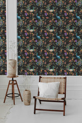 A room with black wallpaper adorned with vibrantly colored exotic birds perched on delicate branches surrounded by lush foliage. The intricate design adds an elegant and classic vibe to the space, complementing the natural textures of the wooden furniture and pottery. Traditional wallpaper.