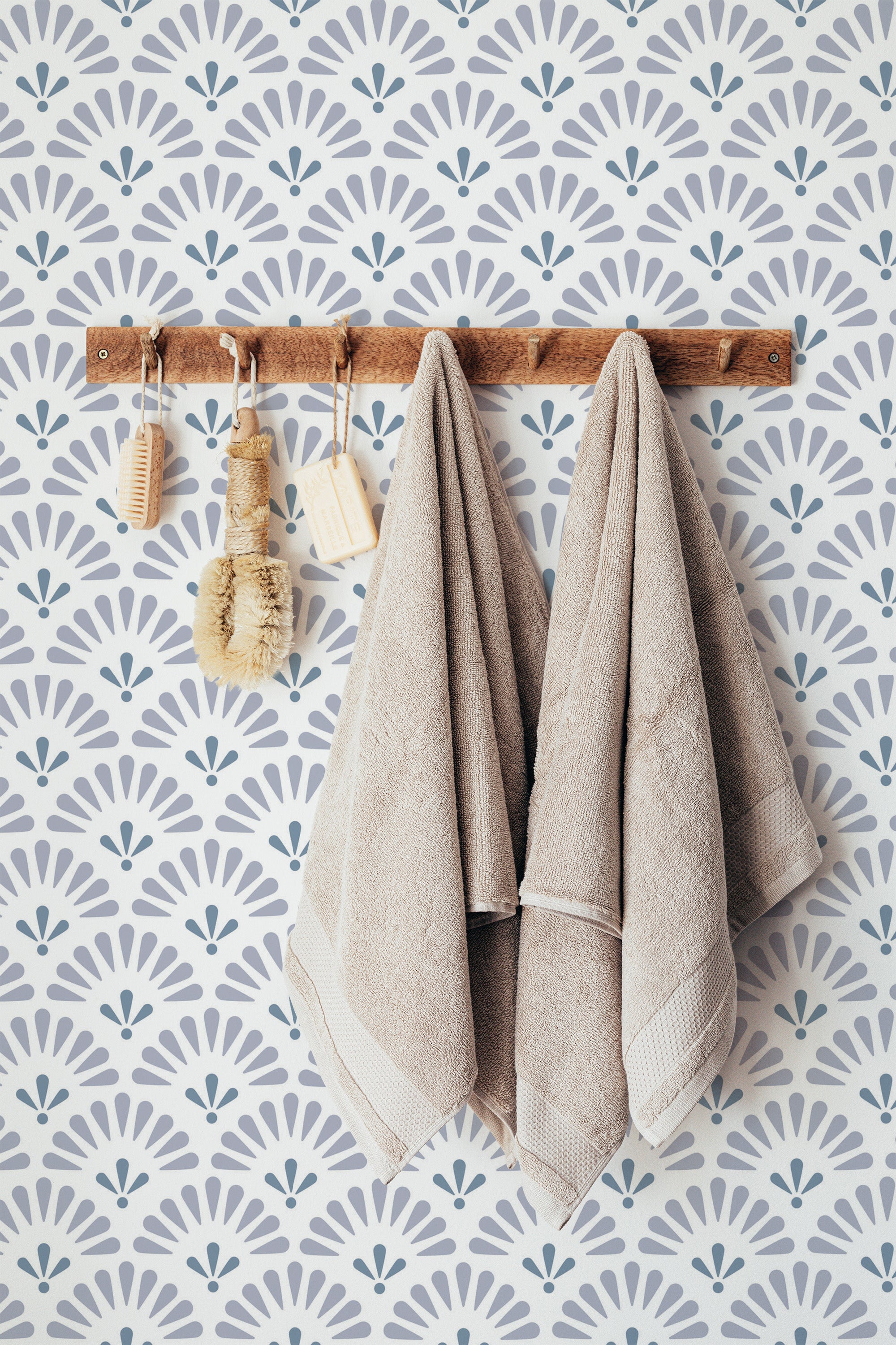 Self-adhesive wallpaper with a retro half-circle pattern in blue and white, creating a fan-like geometric design that adds a vintage touch to the room. The wall features a wooden rack with hanging beige towels and bath accessories.