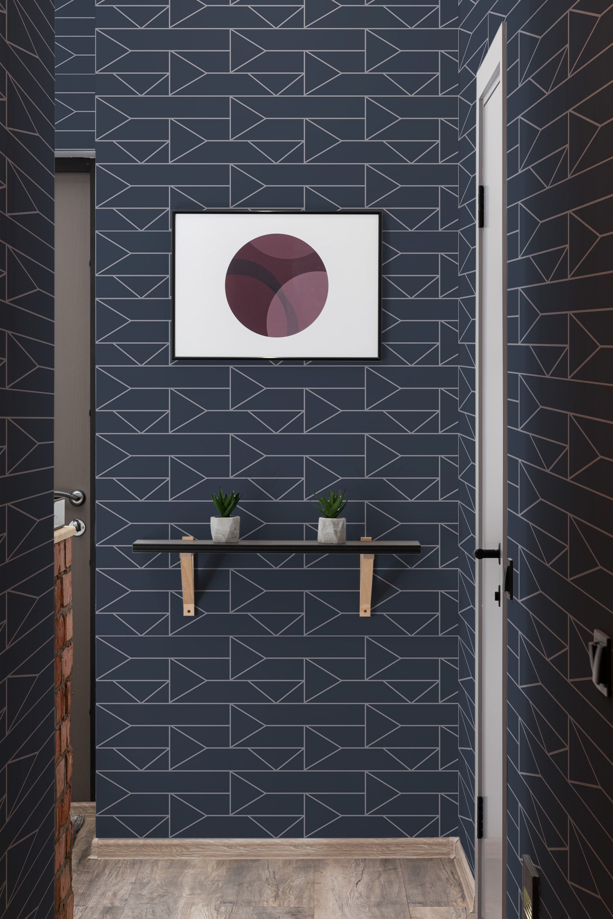 A room with dark blue wallpaper adorned with geometric patterns of triangles and lines in light metallic tones, giving a modern-retro aesthetic. A floating shelf with small plants and a framed abstract artwork hangs on the wall, complementing the clean and minimalistic design of the traditional wallpaper.