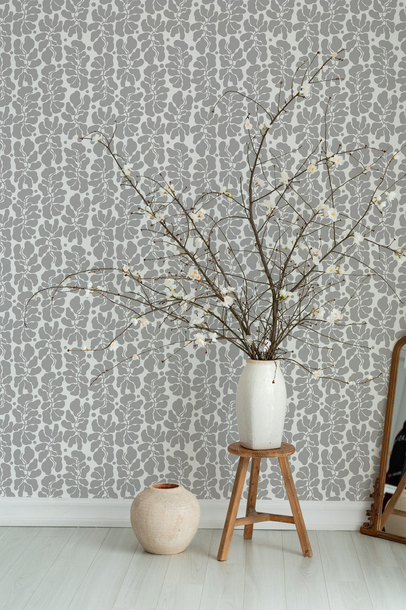 Self-adhesive wallpaper with an abstract leaf pattern in shades of grey on a room's wall, with a vase of dried branches on a wooden stool and another pot beside it.