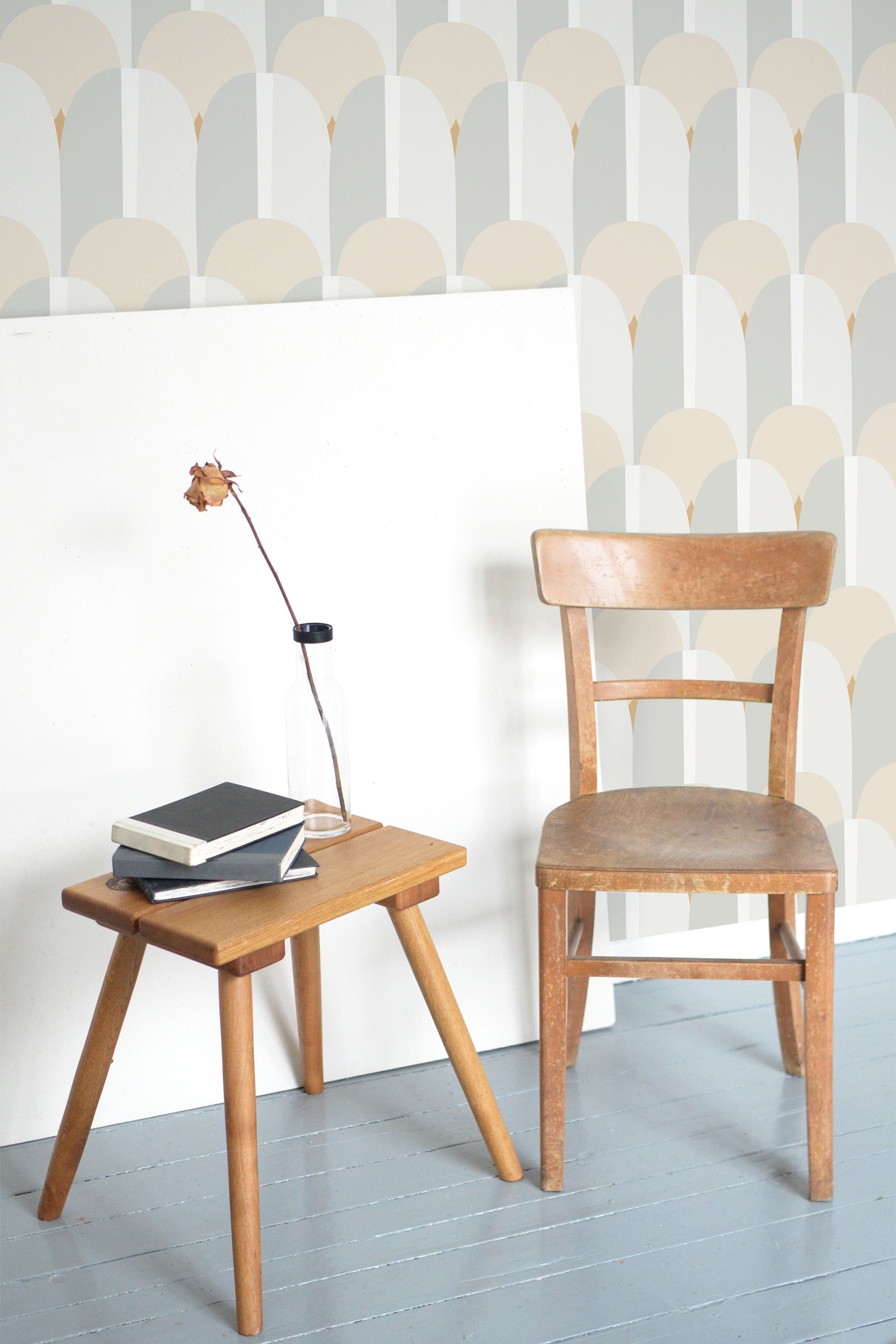 Self-adhesive pastel Art Deco wallpaper with geometric half-circle pattern in soft tones on a room wall with a wooden chair and side table.
