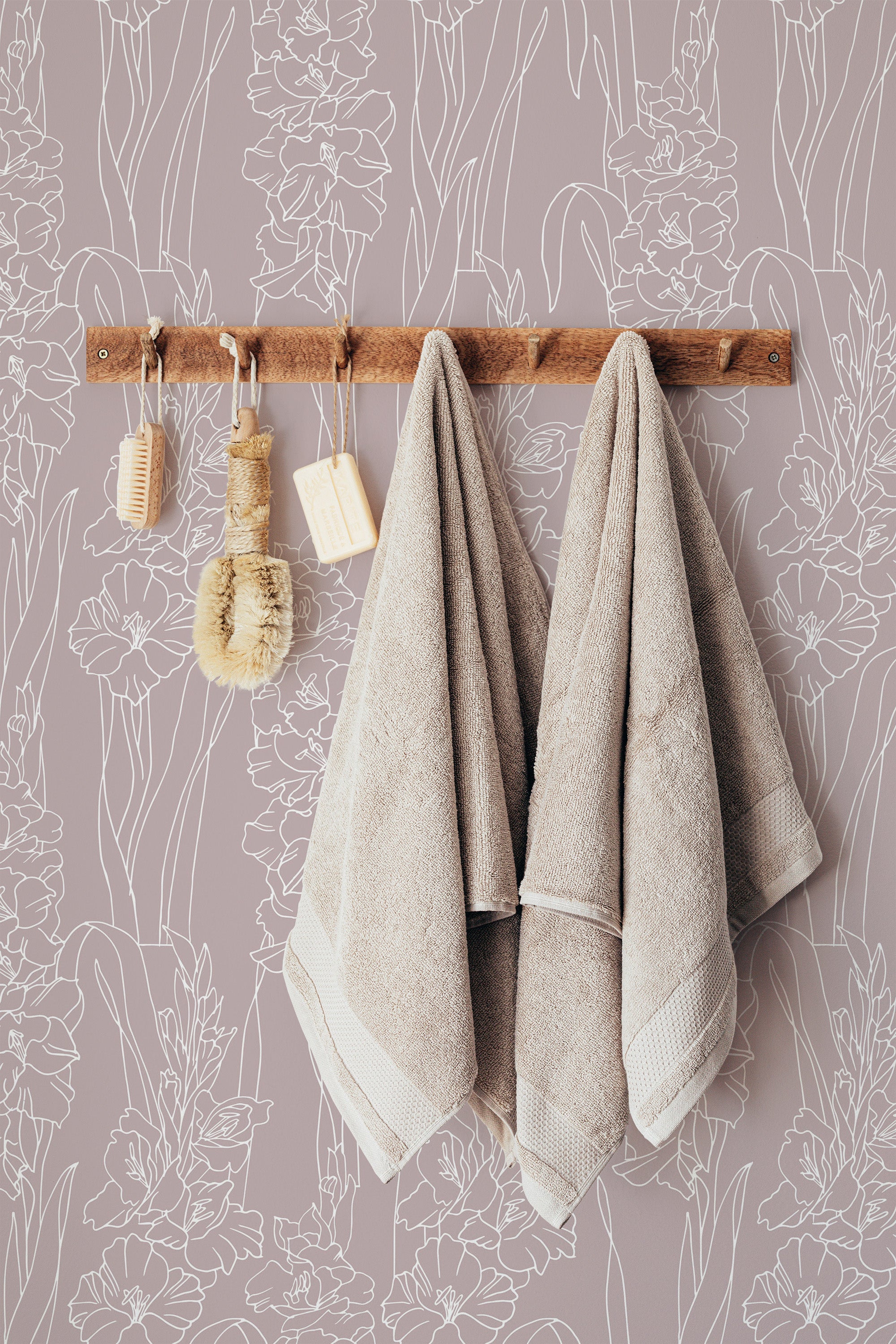 Self-adhesive wallpaper with a white gladiolus pattern on a muted purple background, with towels hanging on a wooden rack in front.