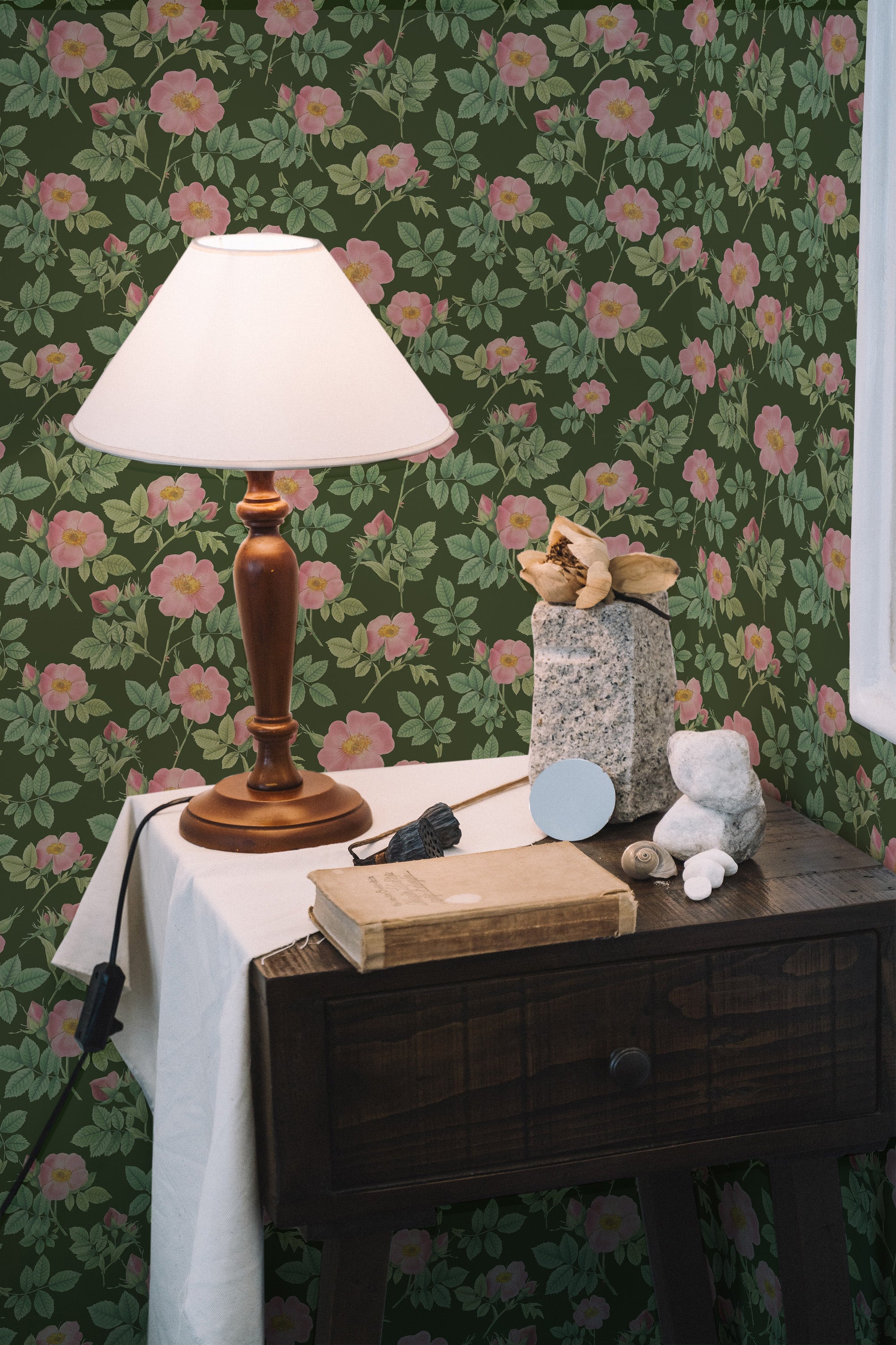 Self-adhesive wallpaper with a bold rose pattern on a green background, complemented by a wooden desk, lamp, and decorative items.