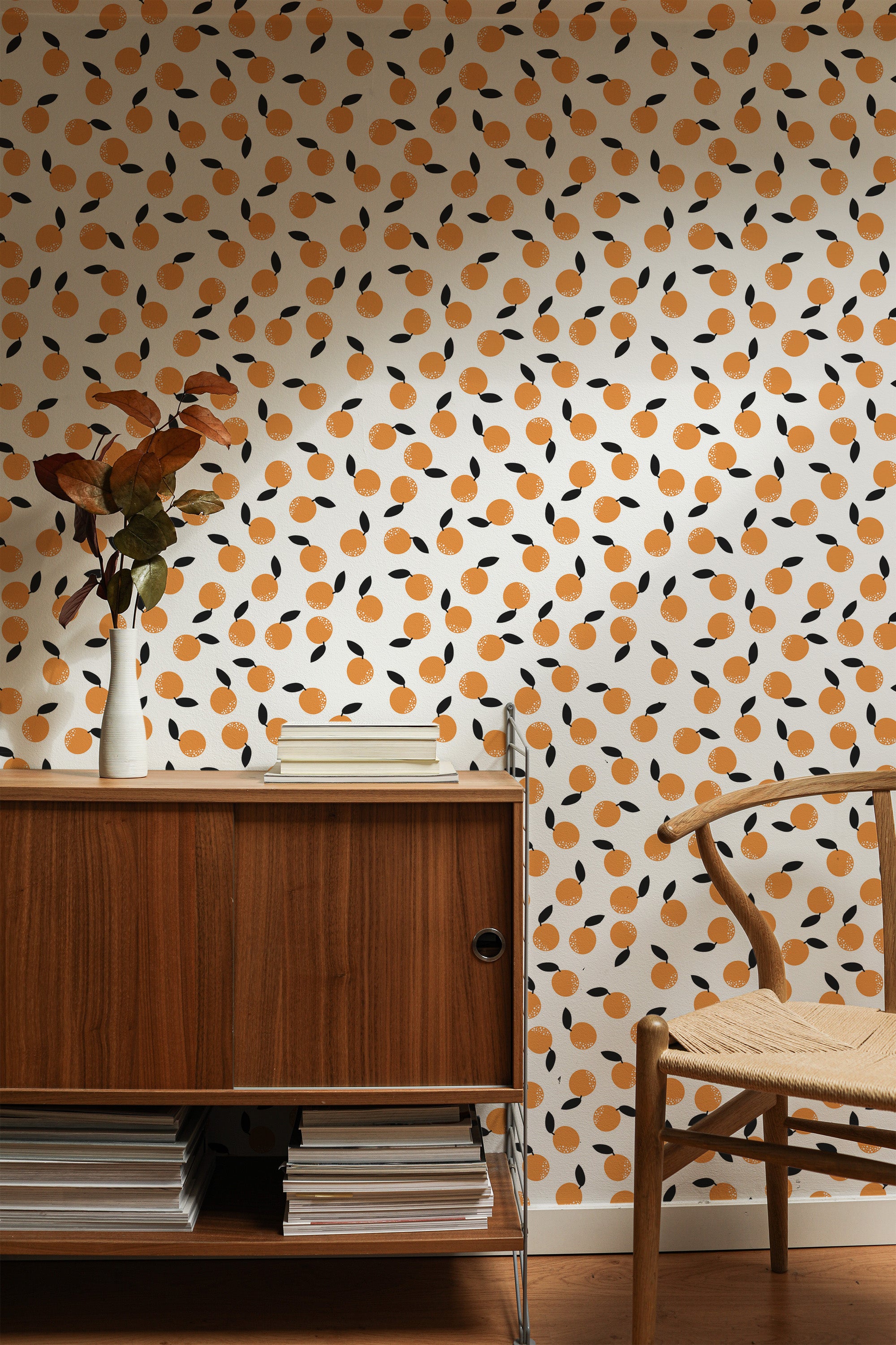 Self-adhesive wallpaper with orange fruit pattern on a cream background, accented by black and taupe splashes, in a stylish room with wooden furniture.