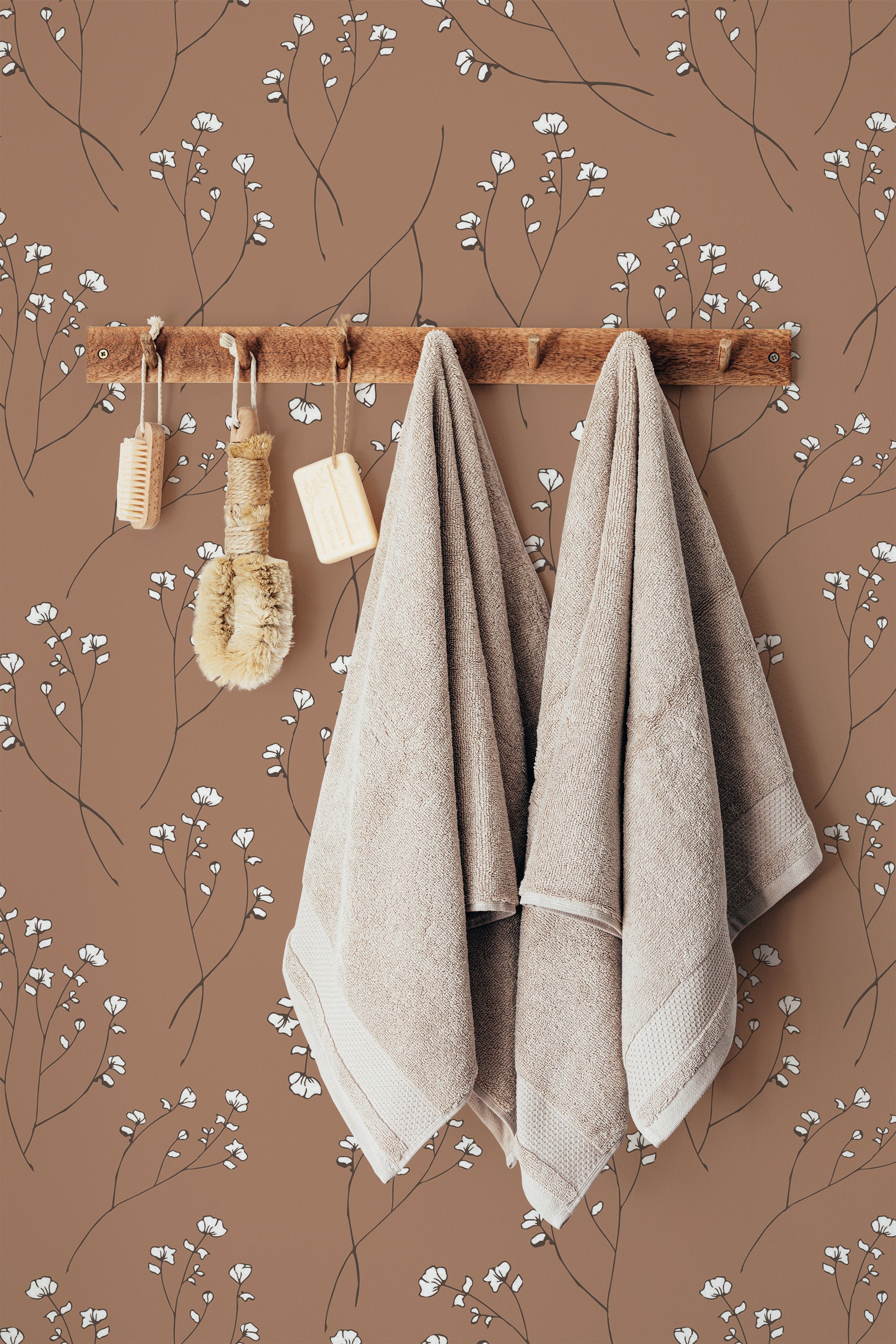 Self-adhesive delicate neutral floral wallpaper with white flower patterns on a brown background, accompanied by wooden hangers and beige towels.