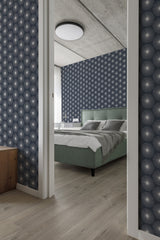 A bedroom with a wall covered in dark blue traditional wallpaper with a stylized dandelion pattern, complementing a green bed and wooden furniture.