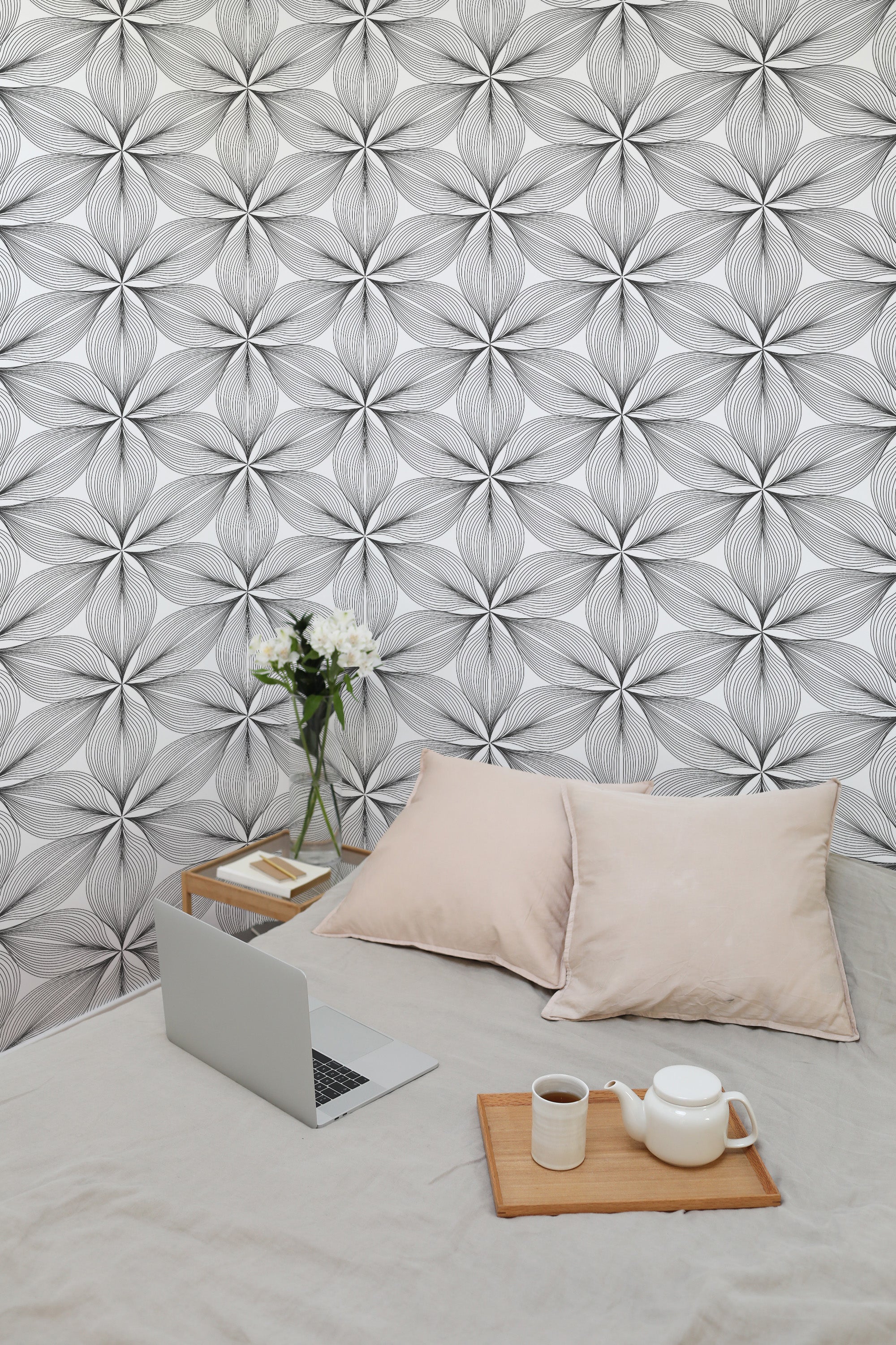 Self-adhesive wallpaper with a monochromatic striped flower pattern, accompanied by a cozy seating area with cushions, a laptop, and a tea set.