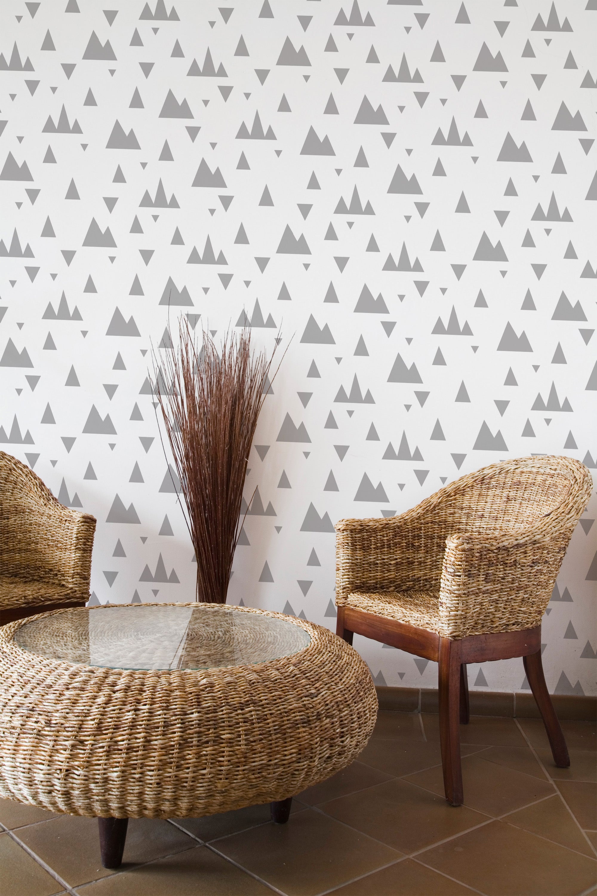 Self-adhesive geometric mountain wallpaper with a repeating pattern of gray and white triangles on a wall, accompanied by wicker furniture and a bouquet of dry branches.