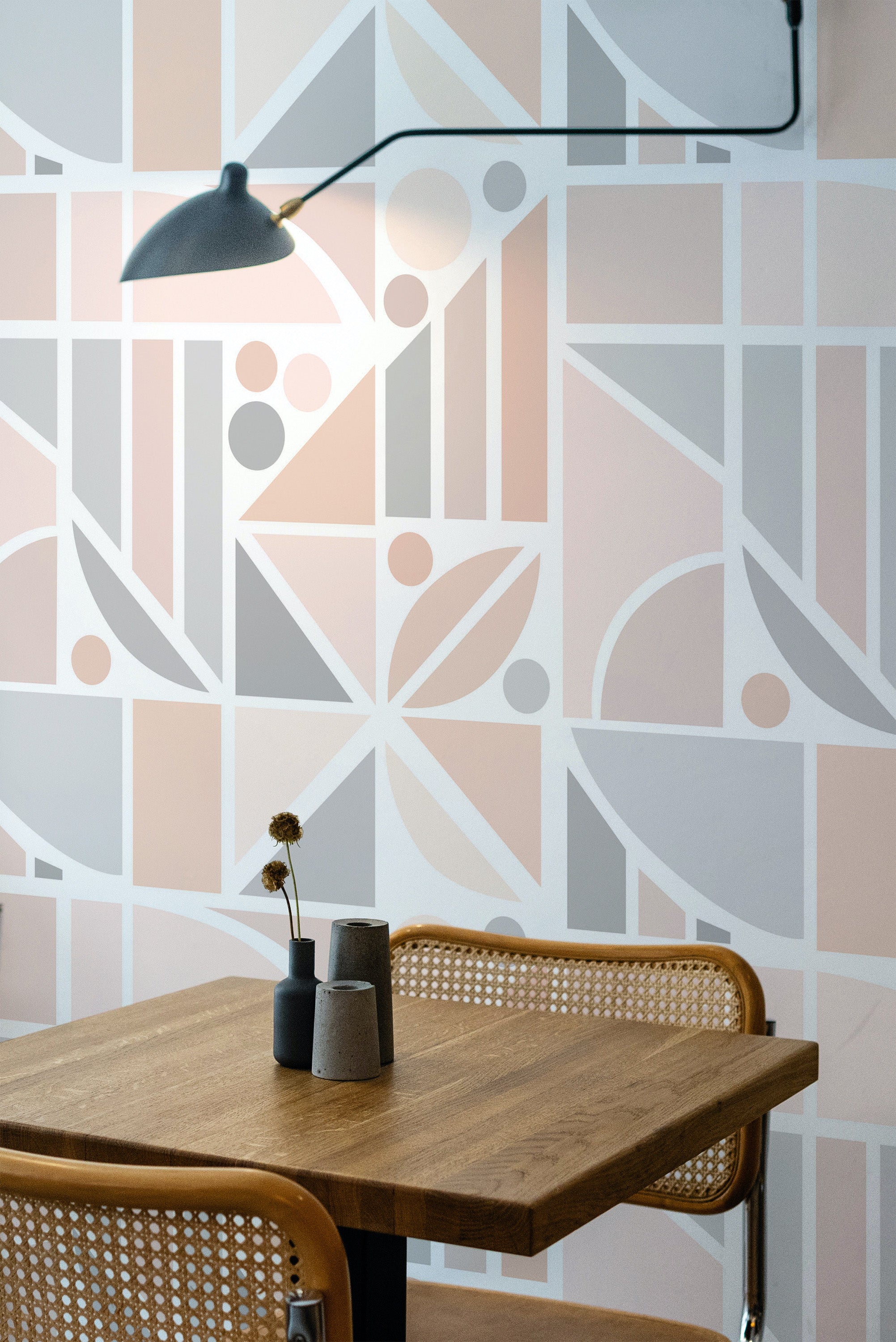 Self-adhesive pastel tile wallpaper with geometric shapes and lines in soft pink and grey hues, creating a modern and clean aesthetic in a room with a wooden table and chair.