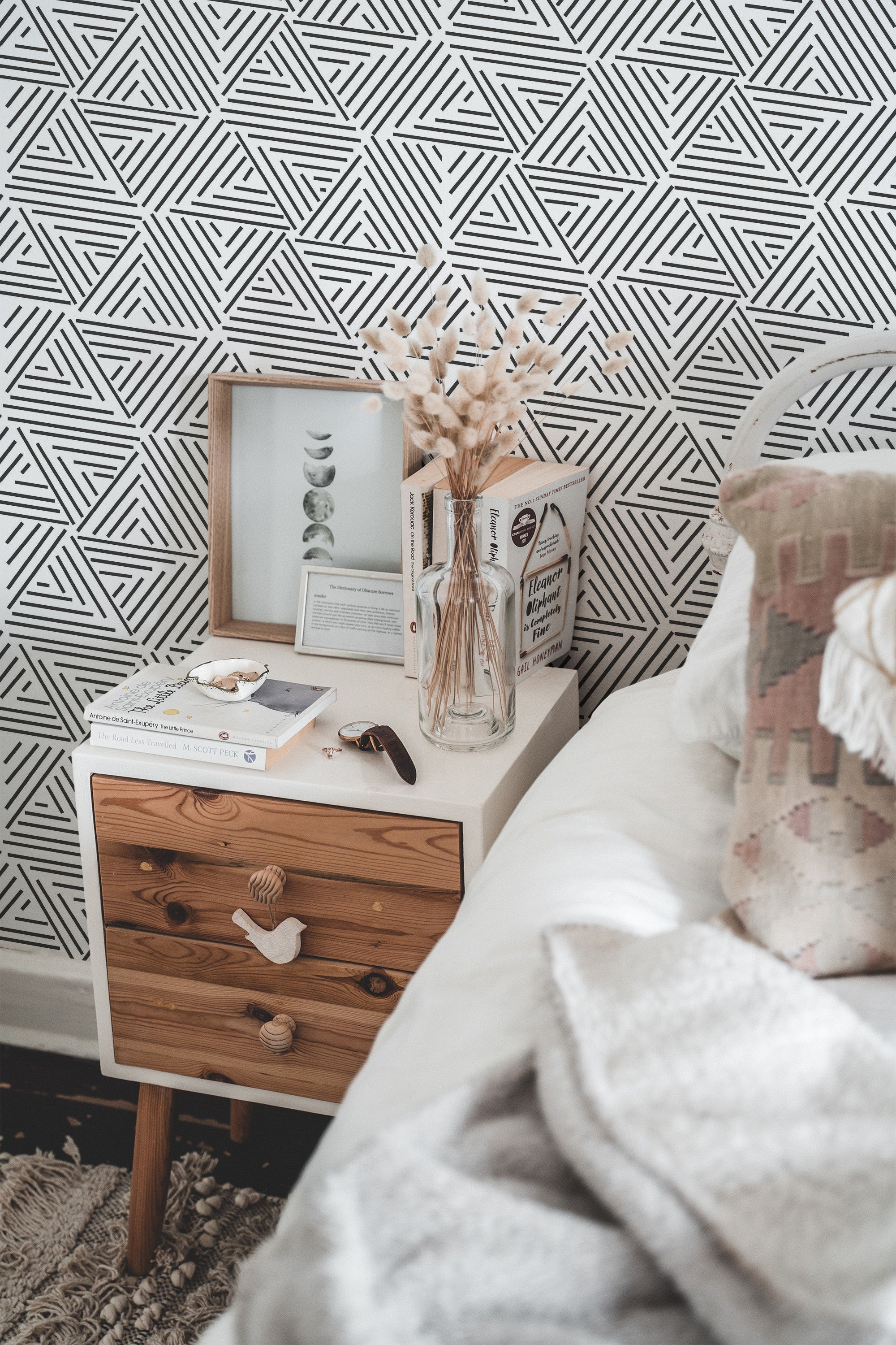 Self-adhesive wallpaper with a geometric striped triangle pattern in black and white on a wall behind a nightstand with decorative items.
