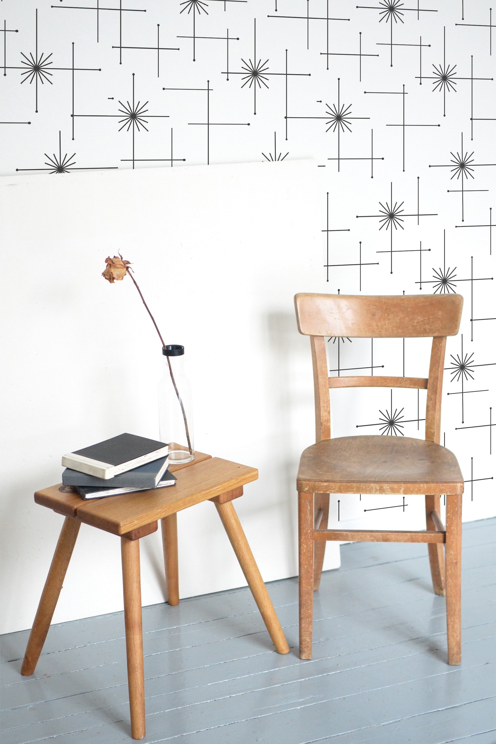 Self-adhesive wallpaper with a seamless star pattern on a light wall, beside a wooden chair and table with a lamp and books.