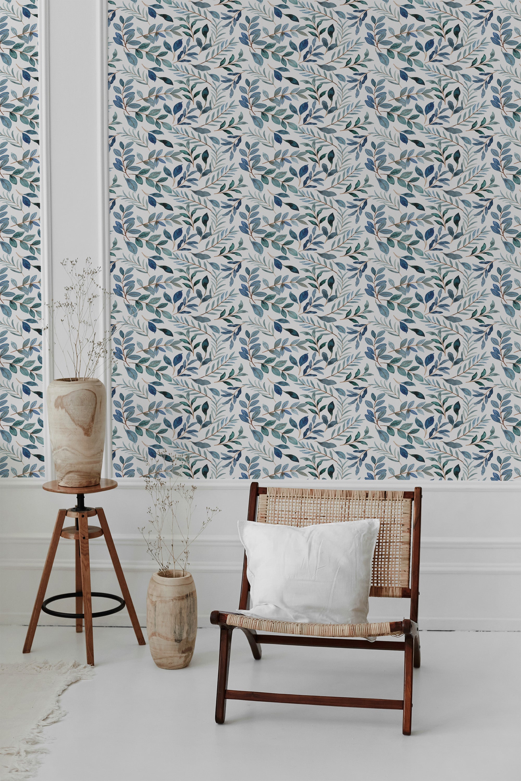 A room with a wall covered in Blue watercolor Leaf wallpaper with a pattern of blue and green leaves, alongside furniture and a potted plant, evoking a serene ambiance with traditional wallpaper.