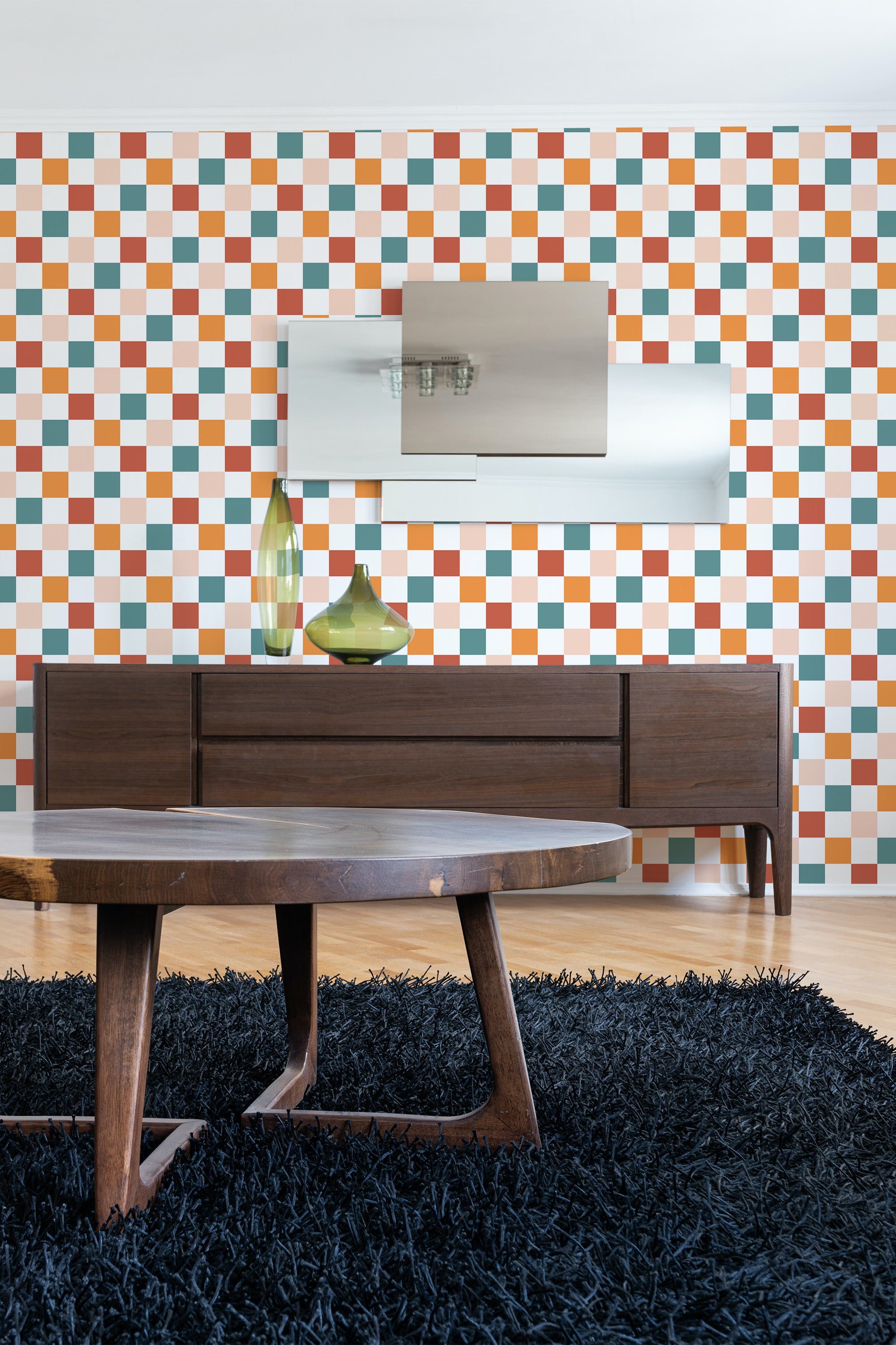 A room with colorful check-patterned wallpaper in shades of orange, green, and white, above a wooden credenza with a mirror and vases, ending with a shaggy black rug, traditional wallpaper.