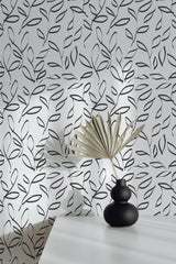 Self-adhesive wallpaper with a black and white painted leaf pattern on a wall, accompanied by a decorative fan and a black vase on a white surface.