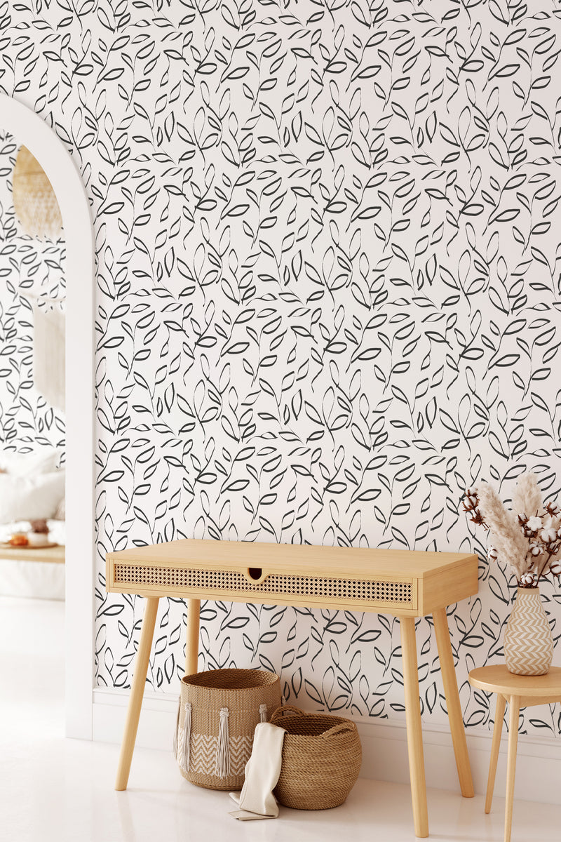 A bright room with a wall covered in wallpaper with a black and white painted leaf pattern, complemented by minimalistic furniture, embodying a traditional wallpaper style.