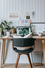 Self-adhesive wavy stripe wallpaper in a room with notes and illustrations pinned above a desk with a computer and chair.