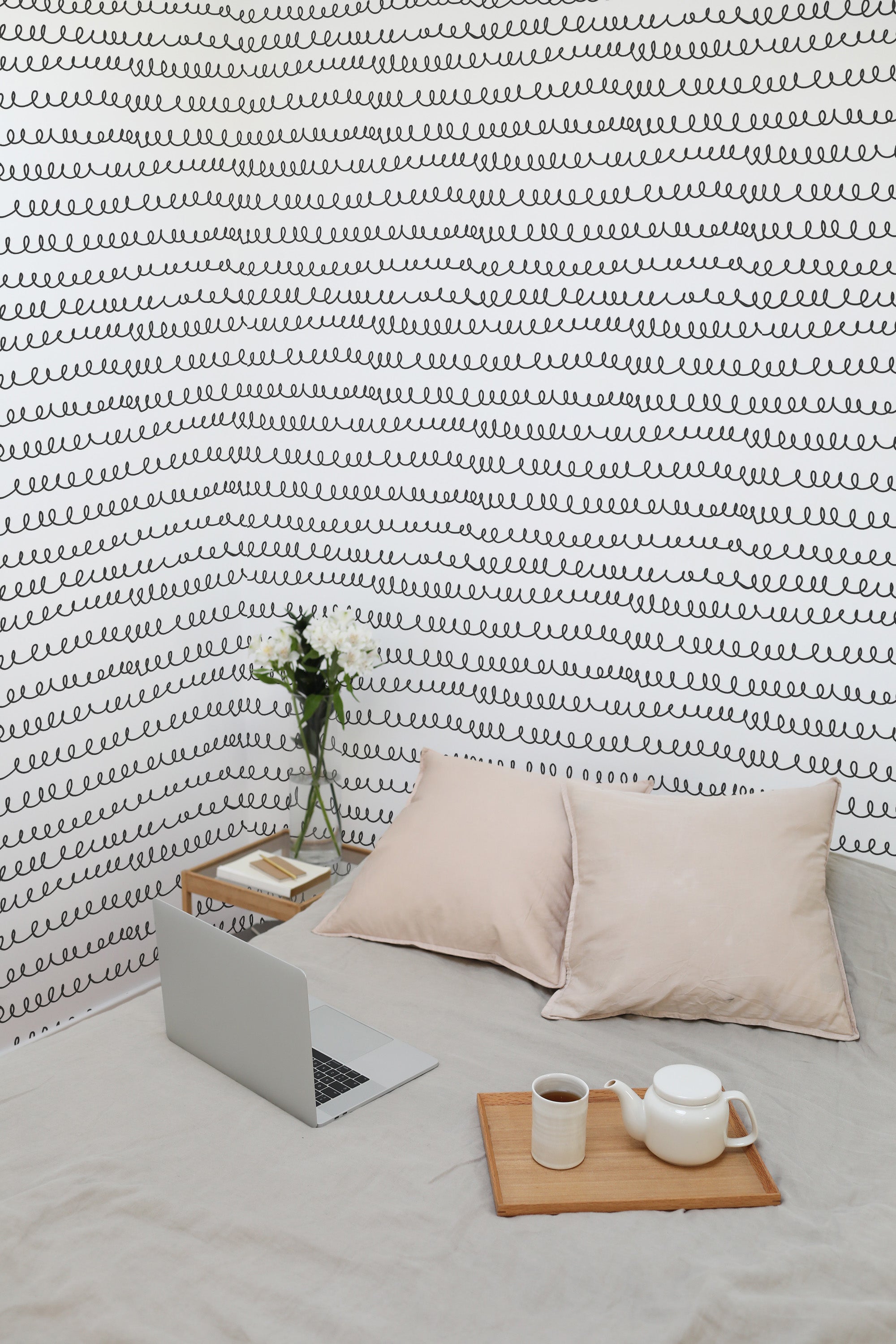 Self-adhesive wallpaper with a repeating black spiral line pattern on a white background, covering a room's wall with home office setup on the floor.