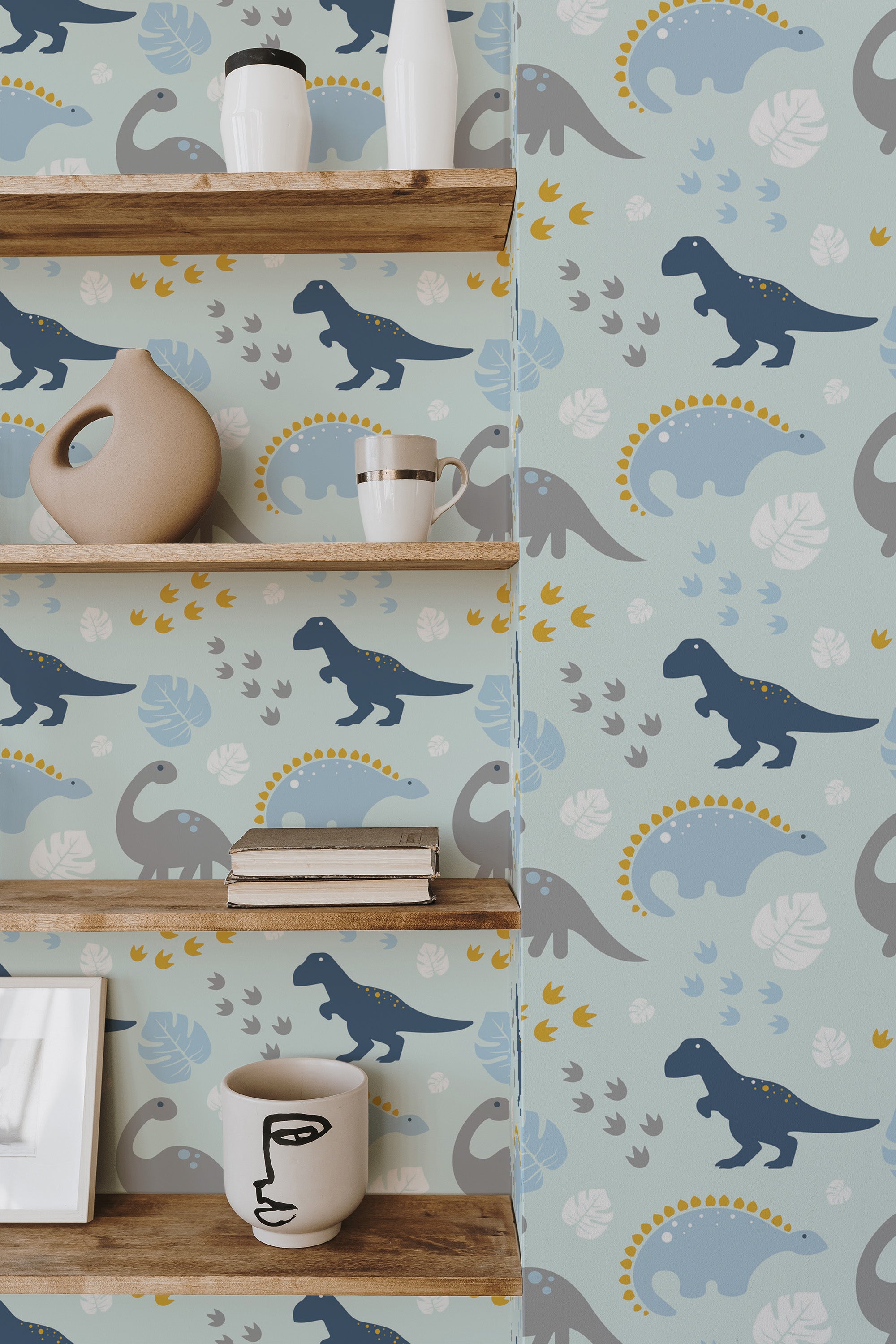 Self-adhesive wallpaper with a blue dinosaur pattern on a beige background, interspersed with grey leaves and pale blue dots, accented by wooden shelves with decorative items.