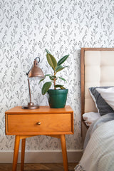 Self-adhesive minimalist floral wallpaper with simple black and grey plant patterns on a white background, in a room with wooden bedside table and bed.