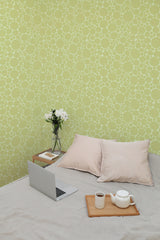 Self-adhesive wallpaper with a pattern of green spots on the walls in a room with a laptop, cushions, a tea set, and a vase with flowers on a bed.