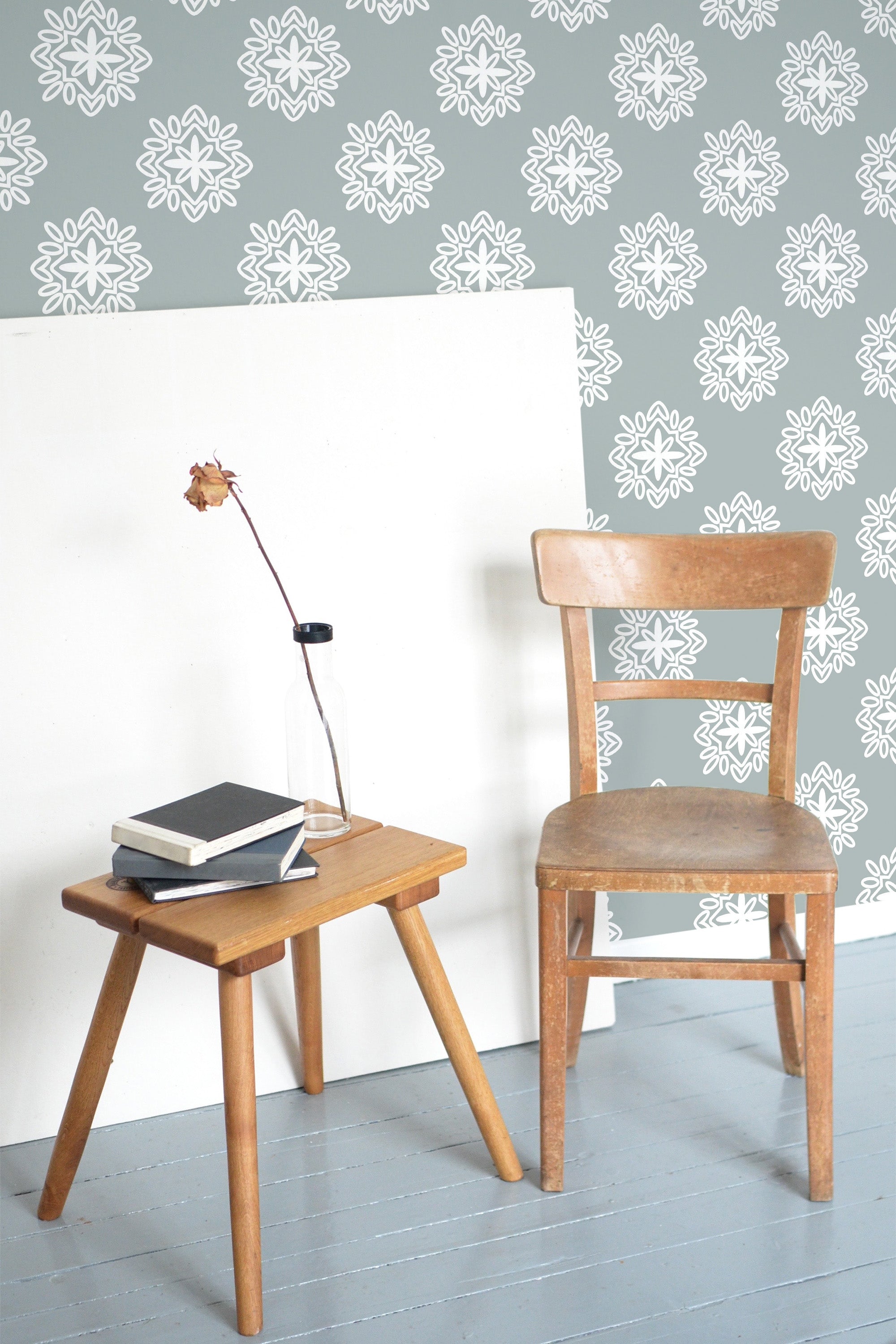 Self-adhesive retro ornamental wallpaper with white floral patterns on a soft blue background in a room with a wooden chair and stool.