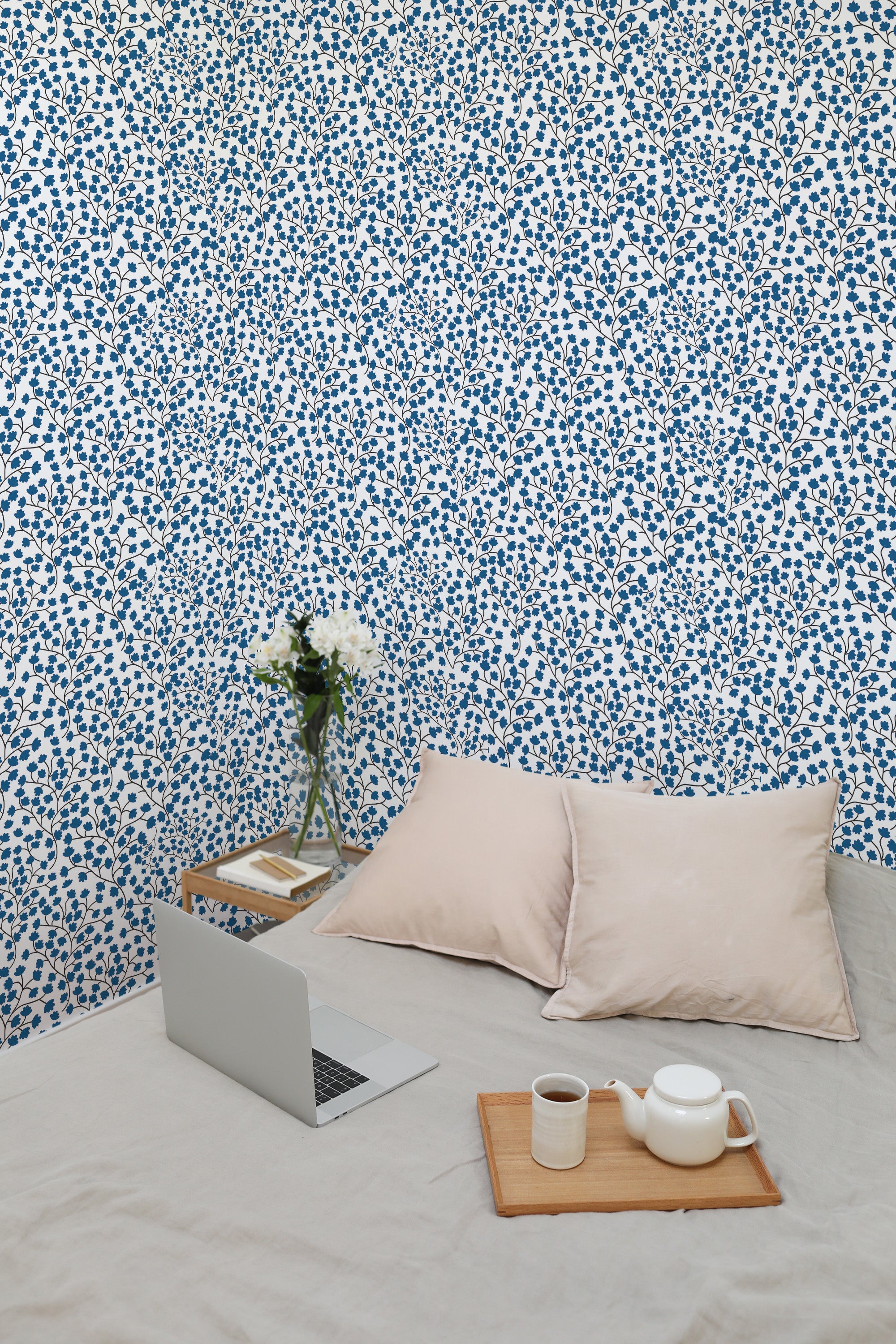 Self-adhesive Tiny blue floral wallpaper with small blue flowers spread evenly on a white background, in a room with a bed and laptop.