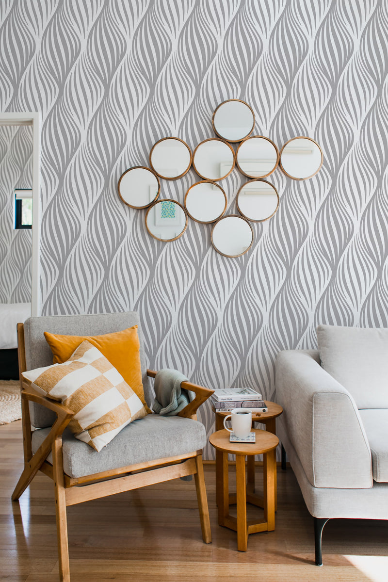 A cozy room corner with a wooden armchair and plush sofa, complemented by a unique wall adorned with abstract leaf stripe wallpaper in a soft gray and white color scheme, adding an elegant touch of traditional wallpaper.