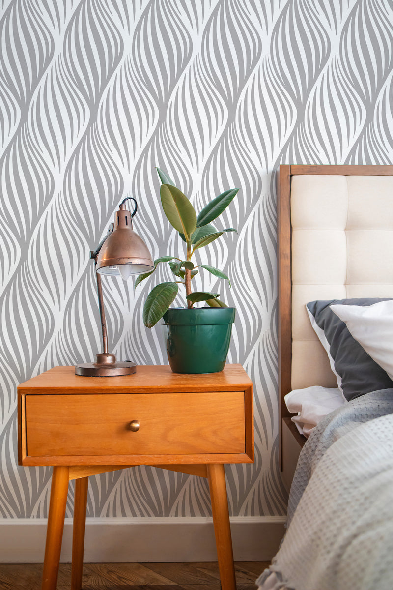 Self-adhesive wallpaper with an abstract leaf stripe design in a bedroom, accompanied by a wooden bedside table, a lamp, and a plant.