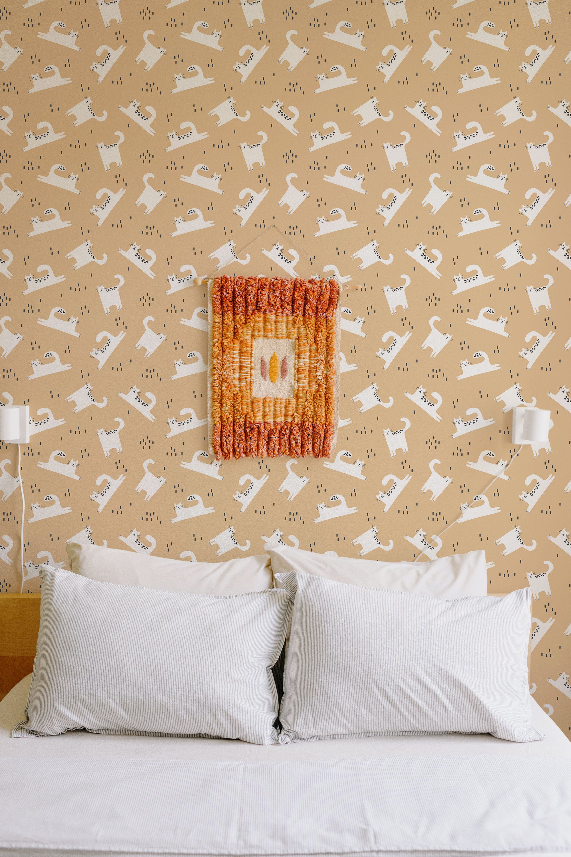Self-adhesive wallpaper with repeating pattern of playful white cat silhouettes on a beige background, in a cozy room with a bed and white pillows.