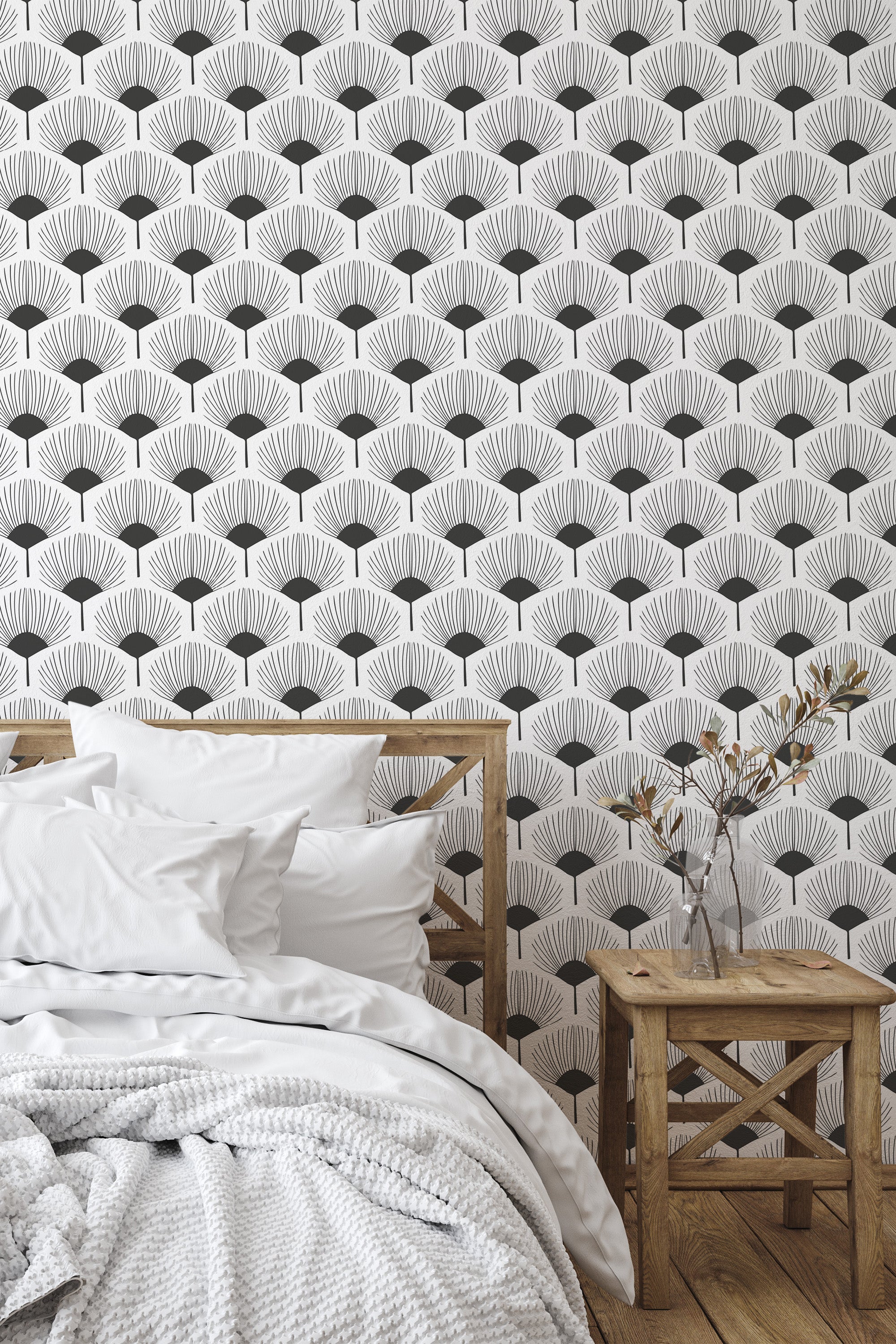 Self-adhesive wallpaper with black and white abstract floral patterns on a bedroom wall above a bed with white bedding and a wooden bedside table.